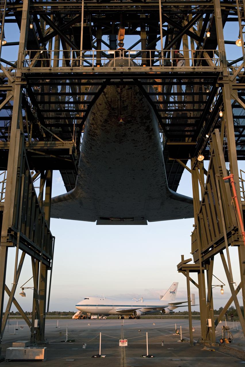 CAPE CANAVERAL, Fla. – At the Shuttle Landing Facility at NASA’s Kennedy Space Center in Florida, space shuttle Discovery is suspended 60 feet off the ground inside the mate-demate device in preparation for the arrival of the Shuttle Carrier Aircraft, in the background.  The device, known as the MDD, is a large gantry-like steel structure used to hoist a shuttle off the ground and position it onto the back of the aircraft, or SCA. The SCA is a Boeing 747 jet, originally manufactured for commercial use, which was modified by NASA to transport the shuttles between destinations on Earth. The SCA designated NASA 905 is assigned to the remaining ferry missions, delivering the shuttles to their permanent public display sites.  NASA 905 is scheduled to ferry Discovery to the Washington Dulles International Airport in Virginia on April 17, after which the shuttle will be placed on display in the Smithsonian's National Air and Space Museum Steven F. Udvar-Hazy Center. For more information on the SCA, visit http://www.nasa.gov/centers/dryden/news/FactSheets/FS-013-DFRC.html. For more information on shuttle transition and retirement activities, visit http://www.nasa.gov/transition.  Photo credit: NASA/Dimitri Gerondidakis