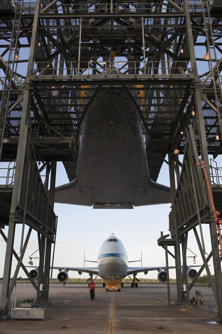 CAPE CANAVERAL, Fla. – At the Shuttle Landing Facility at NASA’s Kennedy Space Center in Florida, space shuttle Discovery is suspended 60 feet off the ground inside the mate-demate device in preparation for the arrival of the Shuttle Carrier Aircraft, in the background.      The device, known as the MDD, is a large gantry-like steel structure used to hoist a shuttle off the ground and position it onto the back of the aircraft, or SCA. The SCA is a Boeing 747 jet, originally manufactured for commercial use, which was modified by NASA to transport the shuttles between destinations on Earth. This SCA, designated NASA 905, is assigned to the remaining ferry missions, delivering the shuttles to their permanent public display sites.  NASA 905 is scheduled to ferry Discovery to the Washington Dulles International Airport in Virginia on April 17, after which the shuttle will be placed on display in the Smithsonian's National Air and Space Museum Steven F. Udvar-Hazy Center. For more information on the SCA, visit http://www.nasa.gov/centers/dryden/news/FactSheets/FS-013-DFRC.html. For more information on shuttle transition and retirement activities, visit http://www.nasa.gov/transition. Photo credit: NASA/Dimitri Gerondidakis
