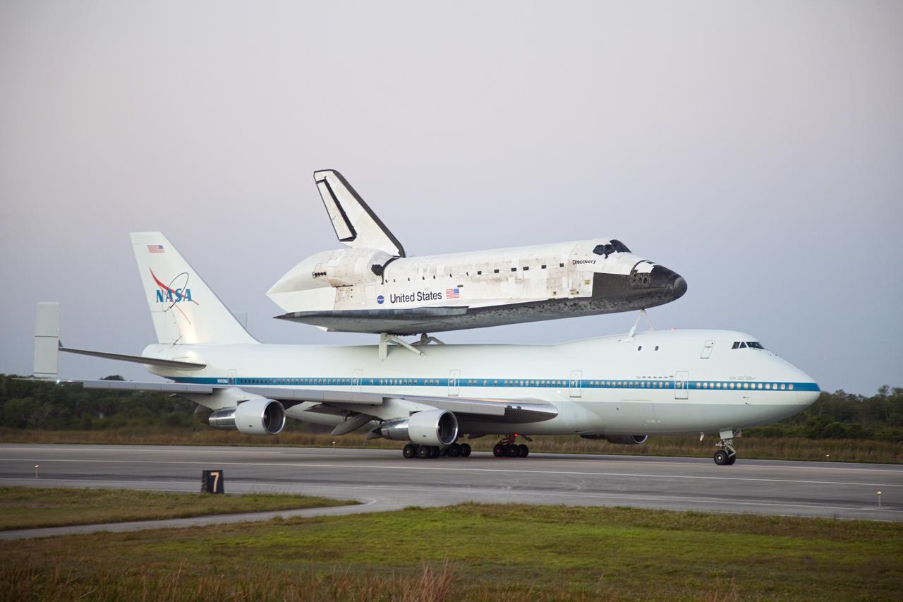 CAPE CANAVERAL, Fla. – Space shuttle Discovery, mounted to a Shuttle Carrier Aircraft, slowly rolls along the runway of the Shuttle Landing Facility at NASA's Kennedy Space Center in Florida. The duo is set to begin their 3 1/2 hour ferry flight to the Washington Dulles International Airport in Virginia at about 7 a.m. EDT. Above the two craft is a NASA helicopter covering the departure. Discovery is leaving Kennedy after more than 28 years of service beginning with its arrival on the space coast Nov. 9, 1983. Discovery first launched to space Aug. 30, 1984, on the STS-41D mission. Discovery is the agency's most-flown shuttle with 39 missions, more than 148 million miles and a total of one year in space. Discovery is set to move to the Smithsonian's National Air and Space Museum Steven F. Udvar-Hazy Center on April 19 where it will be placed on public display. For more information on the SCA, visit http://www.nasa.gov/centers/dryden/news/FactSheets/FS-013-DFRC.html. For more information on shuttle transition and retirement activities, visit http://www.nasa.gov/transition. Photo credit: NASA/Frankie Martin