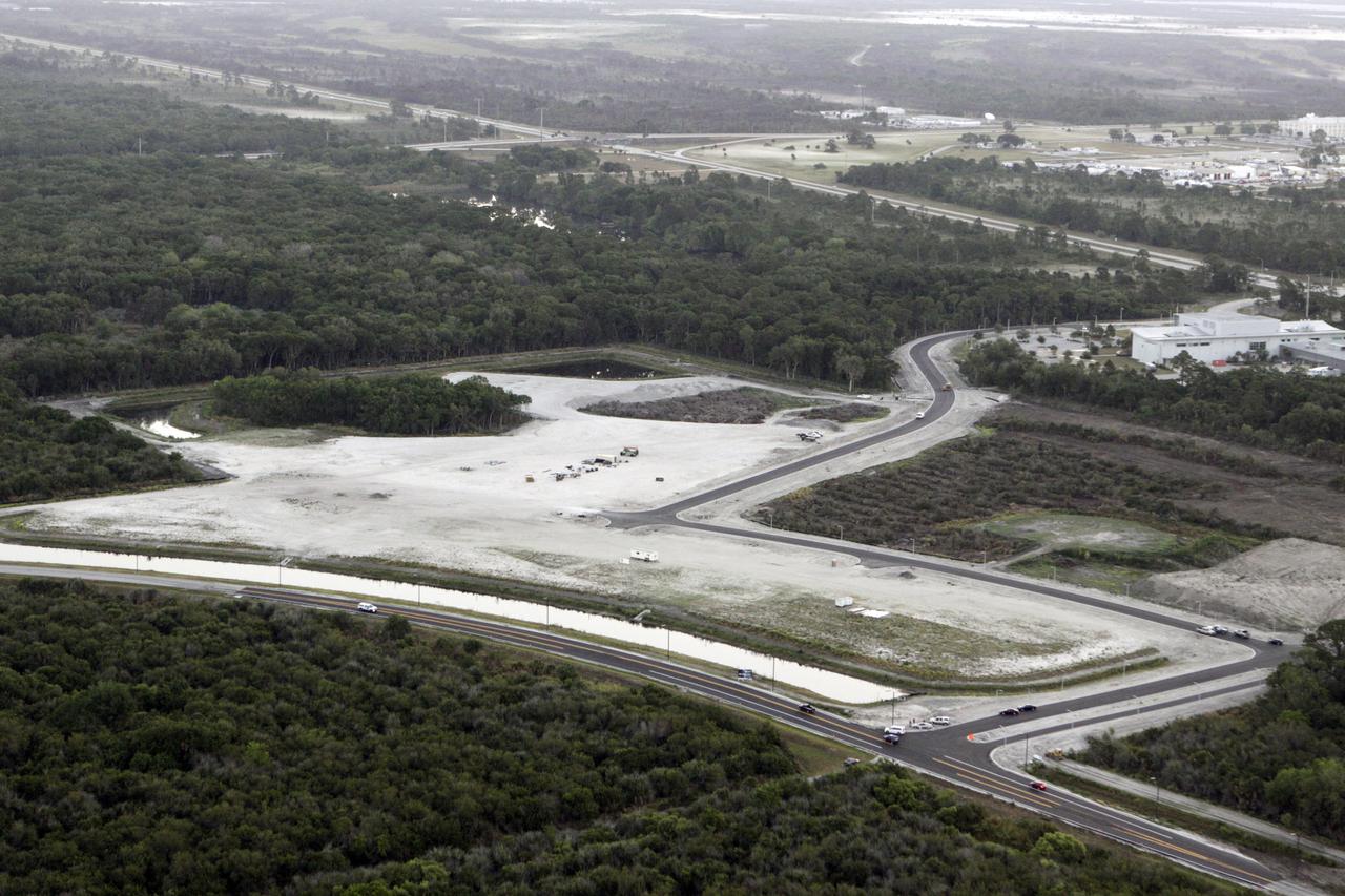 CAPE CANAVERAL, Fla. – This aerial view over NASA’s Kennedy Space Center in Florida reveals a new road winding its way from Space Commerce Way, in the foreground, past the construction site for the new Exploration Park, to the Space Life Sciences Laboratory SLSL, at right.  In the background, at far right, is Kennedy’s Industrial Area.    The land was cleared for the first phase of construction following the park’s groundbreaking in June 2010. The park encompasses 60 acres just outside Kennedy’s security gates near the Kennedy Space Center Visitor Complex. Exploration Park is designed to be a strategically located complex, adjacent to the SLSL, for servicing diverse tenants and uses that will engage in activities to support the space-related activities of NASA, other government agencies and the U.S. commercial space industry, as well as attract new aerospace work to the Space Coast. Its nine sustainable, state-of-the-art buildings will include educational, office, research and laboratory, and high-bay facilities and provide 350,000-square feet of work space. Each building is expected to qualify for the U.S. Green Building Council’s Leadership in Environmental and Energy Design LEED certification. The SLSL will be the anchor facility for the park. Photo credit: NASA/Glenn Benson