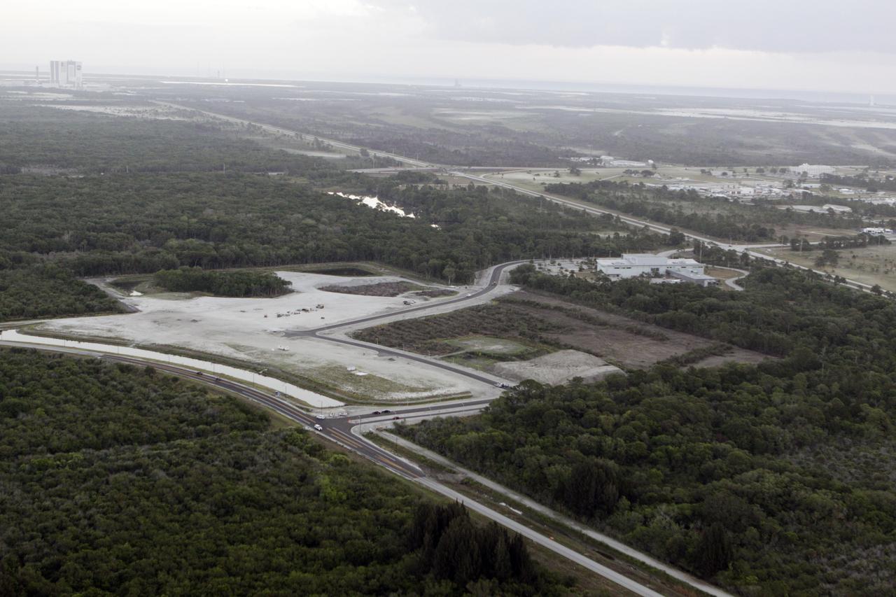 CAPE CANAVERAL, Fla. – This aerial view over NASA’s Kennedy Space Center in Florida reveals a new road winding its way from Space Commerce Way, in the foreground, past the construction site for the new Exploration Park, to the Space Life Sciences Laboratory SLSL.  At right is Kennedy’s Industrial Area.  Spanning the background is the Atlantic Ocean. In the distance, the facilities in Launch Complex 39 are, from left, the Vehicle Assembly Building, Pad 39B, Pad 39A, and Space Launch Complex-41 on Cape Canaveral Air Force Station.      The land was cleared for the first phase of construction following the park’s groundbreaking in June 2010. The park encompasses 60 acres just outside Kennedy’s security gates near the Kennedy Space Center Visitor Complex. Exploration Park is designed to be a strategically located complex, adjacent to the SLSL, for servicing diverse tenants and uses that will engage in activities to support the space-related activities of NASA, other government agencies and the U.S. commercial space industry, as well as attract new aerospace work to the Space Coast. Its nine sustainable, state-of-the-art buildings will include educational, office, research and laboratory, and high-bay facilities and provide 350,000-square feet of work space. Each building is expected to qualify for the U.S. Green Building Council’s Leadership in Environmental and Energy Design LEED certification. The SLSL will be the anchor facility for the park. Photo credit: NASA/Glenn Benson