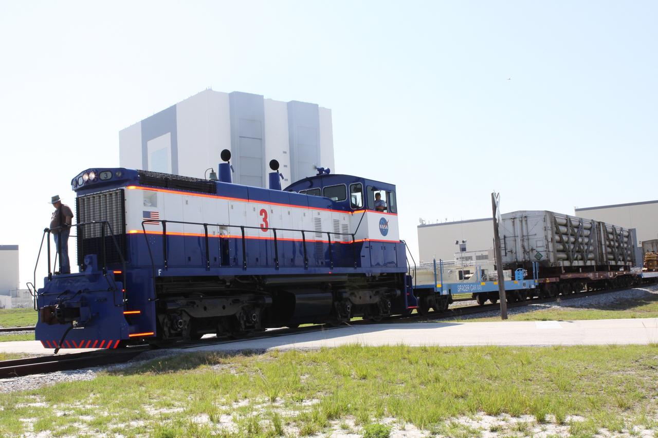 CAPE CANAVERAL, Fla. – A NASA Railroad train passes in front of the 525-foot-tall Vehicle Assembly Building, left, and the twin bays of the Orbiter Processing Facility, right, at NASA’s Kennedy Space Center in Florida.  The train is on its way to the Florida East Coast Railway interchange in Titusville, Fla., where the train’s helium tank cars, a liquid oxygen tank car, and a liquid hydrogen dewar or tank car will be transferred for delivery to the SpaceX engine test complex outside McGregor, Texas.    The railroad cars were needed in support of the Space Shuttle Program but currently are not in use by NASA following the completion of the program in 2011. Originally, the tankers belonged to the U.S. Bureau of Mines.  At the peak of the shuttle program, there were approximately 30 cars in the fleet.  About half the cars were returned to the bureau as launch activity diminished. Five tank cars are being loaned to SpaceX and repurposed to support their engine tests in Texas. Eight cars previously were shipped to California on loan to support the SpaceX Falcon 9 rocket launches from Space Launch Complex-4 on Vandenberg Air Force Base.  SpaceX already has three helium tank cars previously used for the shuttle program at Space Launch Complex-40 on Cape Canaveral Air Force Station in Florida. For more information, visit http://www.nasa.gov/spacex.  Photo credit: NASA/Jim Grossmann