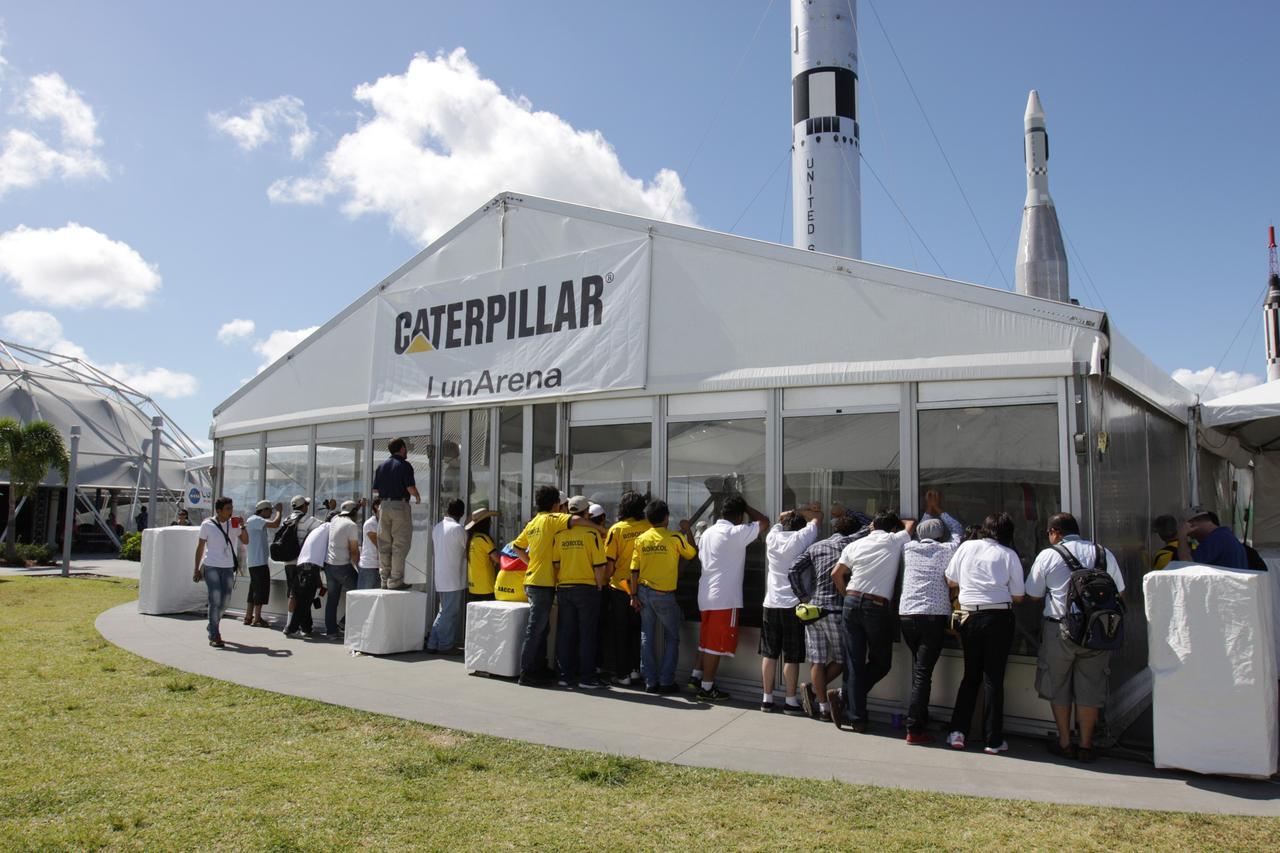 CAPE CANAVERAL, Fla. – Participants watch NASA's Lunabotics Mining Competition at the Kennedy Space Center Visitor Complex in Florida. The competition challenges university students to build machines that can collect soil such as the material found on the moon. Working inside the Caterpillar LunArena, the robotic craft dig soil that simulates lunar material. The event is judged by a machine's abilities to collect the soil, its design and operation, size, dust tolerance and its level of autonomy. Photo credit: NASA/Glenn Benson
