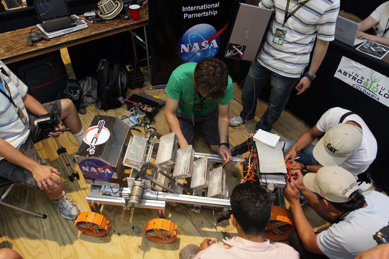CAPE CANAVERAL, Fla. – A team of competitors works with its machine during NASA's Lunabotics Mining Competition at the Kennedy Space Center Visitor Complex in Florida. The competition challenges university students to build machines that can collect soil such as the material found on the moon. Working inside the Caterpillar LunArena, the robotic craft dig soil that simulates lunar material. The event is judged by a machine's abilities to collect the soil, its design and operation, size, dust tolerance and its level of autonomy.  Photo credit: NASA/Glenn Benson