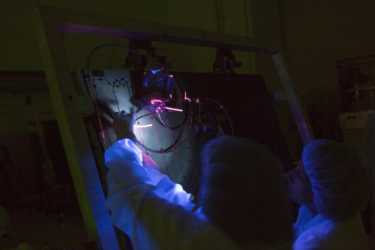 CAPE CANAVERAL, Fla. – Working in near-darkness inside the clean room high bay at the Astrotech payload processing facility near NASA’s Kennedy Space Center in Florida, technicians use black lights to inspect a solar panel on one of NASA's twin Radiation Belt Storm Probes. The technicians are dressed in clean-room attire known as “bunny suits.”    Black-light inspection uses UVA fluorescence to detect possible microcontamination, small cracks or fluid leaks. The Radiation Belt Storm Probes, or RBSP, mission will help us understand the sun’s influence on Earth and near-Earth space by studying the Earth’s radiation belts on various scales of space and time. RBSP will begin its mission of exploration of Earth's Van Allen radiation belts and the extremes of space weather after its launch aboard a United Launch Alliance Atlas V rocket. Launch is targeted for Aug. 23.   For more information, visit http://www.nasa.gov/rbsp.  Photo credit: NASA/Jim Grossmann