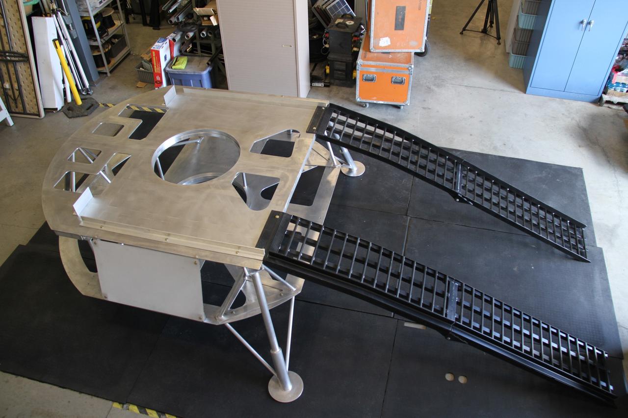 CAPE CANAVERAL, Fla. – The prototype lander for NASA’s Regolith and Environment Science and Oxygen and Lunar Volatile Extraction, or RESOLVE, project is prepared for further assembly in a test facility behind the Operations and Checkout Building at NASA’s Kennedy Space Center in Florida.  The ramps provide RESOLVE’s rover an avenue to mount or dismount the lander.     RESOLVE consists of a rover and drill provided by the Canadian Space Agency to support a NASA payload that is designed to prospect for water, ice and other lunar resources. RESOLVE also will demonstrate how future explorers can take advantage of resources at potential landing sites by manufacturing oxygen from soil. NASA will be conducting field tests in July outside of Hilo, Hawaii, with equipment and concept vehicles that demonstrate how explorers might prospect for resources and make their own oxygen for survival while on other planetary bodies.  For more information, visit http://www.nasa.gov/exploration/analogs/index.html.  Photo credit: NASA/Ben Smegelsky