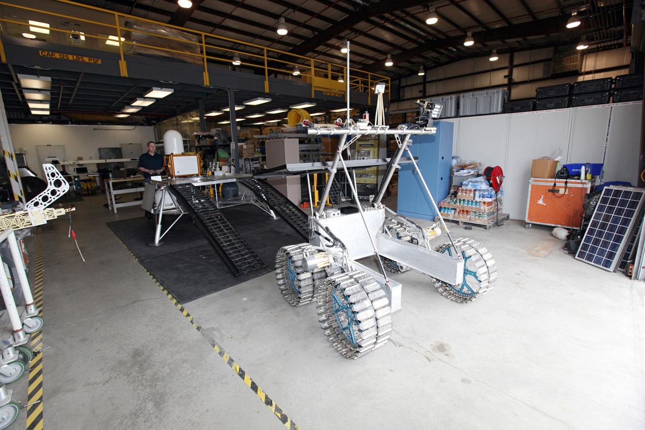 CAPE CANAVERAL, Fla. – In a test facility behind the Operations and Checkout Building at NASA’s Kennedy Space Center in Florida, the prototype rover Artemis Jr. for NASA’s Regolith and Environment Science and Oxygen and Lunar Volatile Extraction, or RESOLVE, project has dismounted the RESOLVE lander during a dry run using the ramps attached to the prototype lander.    RESOLVE consists of a rover and drill provided by the Canadian Space Agency to support a NASA payload that is designed to prospect for water, ice and other lunar resources. RESOLVE also will demonstrate how future explorers can take advantage of resources at potential landing sites by manufacturing oxygen from soil. NASA will conduct field tests in July outside of Hilo, Hawaii, with equipment and concept vehicles that demonstrate how explorers might prospect for resources and make their own oxygen for survival while on other planetary bodies.  For more information, visit http://www.nasa.gov/exploration/analogs/index.html.  Photo credit: NASA/Dimitri Gerondidakis