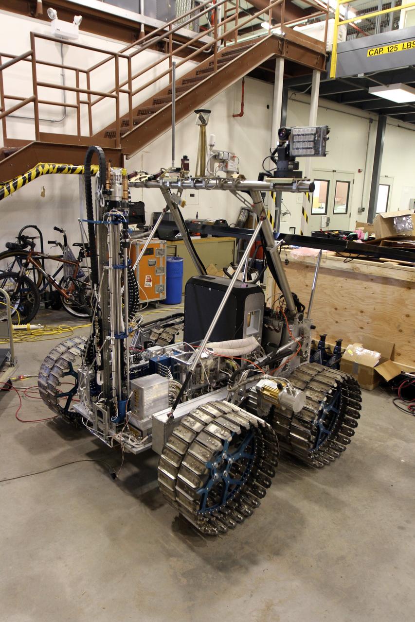 CAPE CANAVERAL, Fla. – The NASA payload is installed on the prototype rover Artemis Jr. for NASA’s Regolith and Environment Science and Oxygen and Lunar Volatile Extraction, or RESOLVE, project in a test facility behind the Operations and Checkout Building at NASA’s Kennedy Space Center in Florida. The cylindrical structure at left is the drill.      The drill and rover were provided to NASA by the Canadian Space Agency. The NASA payload is designed to prospect for water, ice and other lunar resources. RESOLVE also will demonstrate how future explorers can take advantage of resources at potential landing sites by manufacturing oxygen from soil. NASA will conduct field tests in July outside of Hilo, Hawaii, with equipment and concept vehicles that demonstrate how explorers might prospect for resources and make their own oxygen for survival while on other planetary bodies.  For more information, visit http://www.nasa.gov/exploration/analogs/index.html.  Photo credit: NASA/Cory Huston