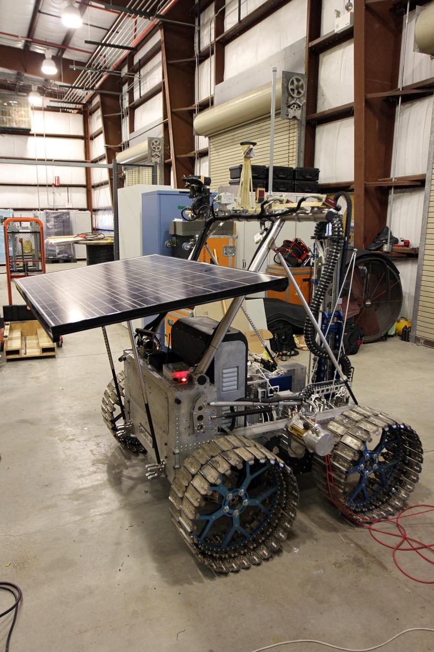 CAPE CANAVERAL, Fla. – The NASA payload is installed on the prototype rover Artemis Jr. for NASA’s Regolith and Environment Science and Oxygen and Lunar Volatile Extraction, or RESOLVE, project in a test facility behind the Operations and Checkout Building at NASA’s Kennedy Space Center in Florida. The cylindrical structure at right is the drill the tabletop surface at left is the rover’s solar array.    The drill and rover were provided to NASA by the Canadian Space Agency. The NASA payload is designed to prospect for water, ice and other lunar resources. RESOLVE also will demonstrate how future explorers can take advantage of resources at potential landing sites by manufacturing oxygen from soil. NASA will conduct field tests in July outside of Hilo, Hawaii, with equipment and concept vehicles that demonstrate how explorers might prospect for resources and make their own oxygen for survival while on other planetary bodies.  For more information, visit http://www.nasa.gov/exploration/analogs/index.html.  Photo credit: NASA/Cory Huston