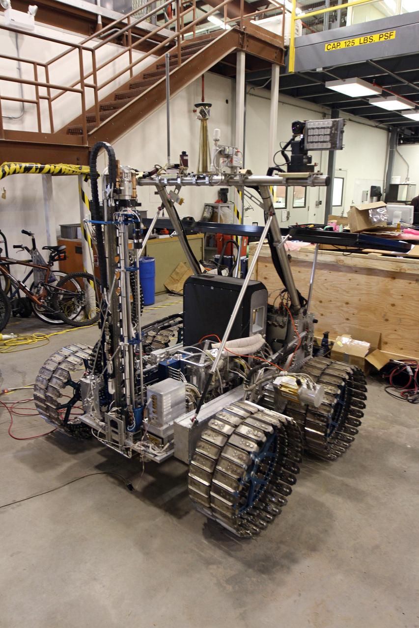 CAPE CANAVERAL, Fla. – The NASA payload is installed on the prototype rover Artemis Jr. for NASA’s Regolith and Environment Science and Oxygen and Lunar Volatile Extraction, or RESOLVE, project in a test facility behind the Operations and Checkout Building at NASA’s Kennedy Space Center in Florida. The cylindrical structure at left is the drill.      The drill and rover were provided to NASA by the Canadian Space Agency. The NASA payload is designed to prospect for water, ice and other lunar resources. RESOLVE also will demonstrate how future explorers can take advantage of resources at potential landing sites by manufacturing oxygen from soil. NASA will conduct field tests in July outside of Hilo, Hawaii, with equipment and concept vehicles that demonstrate how explorers might prospect for resources and make their own oxygen for survival while on other planetary bodies.  For more information, visit http://www.nasa.gov/exploration/analogs/index.html.  Photo credit: NASA/Cory Huston