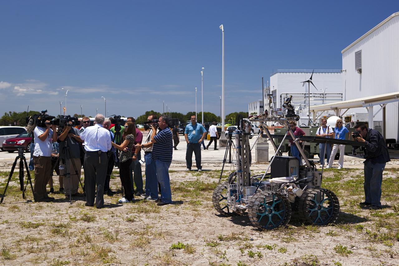 CAPE CANAVERAL, Fla. – NASA In Situ Resource Utilization Project Manager William Larson, back to camera, discusses the design and operation of the prototype rover Artemis Jr. for NASA’s Regolith and Environment Science and Oxygen and Lunar Volatile Extraction, or RESOLVE, project with media representatives during a rover demonstration in a field beside the Operations and Checkout Building at NASA’s Kennedy Space Center in Florida.    The rover and its drill are provided by the Canadian Space Agency and work in concert with NASA science instruments to prospect for water, ice and other lunar resources.  RESOLVE also will demonstrate how future explorers can take advantage of resources at potential landing sites by manufacturing oxygen from soil. NASA will conduct field tests in July outside of Hilo, Hawaii, with equipment and concept vehicles that demonstrate how explorers might prospect for resources and make their own oxygen for survival while on other planetary bodies.  For more information, visit http://www.nasa.gov/exploration/analogs/index.html.  Photo credit: NASA/Dimitri Gerondidakis
