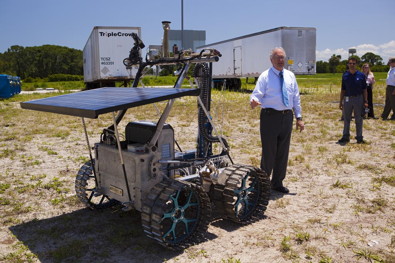 CAPE CANAVERAL, Fla. – NASA In Situ Resource Utilization Project Manager William Larson discusses the design and operation of the prototype rover Artemis Jr. for NASA’s Regolith and Environment Science and Oxygen and Lunar Volatile Extraction, or RESOLVE, project with media representatives during a rover demonstration for media representatives in a field beside the Operations and Checkout Building at NASA’s Kennedy Space Center in Florida.    The rover and its drill are provided by the Canadian Space Agency and work in concert with NASA science instruments to prospect for water, ice and other lunar resources.  RESOLVE also will demonstrate how future explorers can take advantage of resources at potential landing sites by manufacturing oxygen from soil. NASA will conduct field tests in July outside of Hilo, Hawaii, with equipment and concept vehicles that demonstrate how explorers might prospect for resources and make their own oxygen for survival while on other planetary bodies.  For more information, visit http://www.nasa.gov/exploration/analogs/index.html.  Photo credit: NASA/Dimitri Gerondidakis