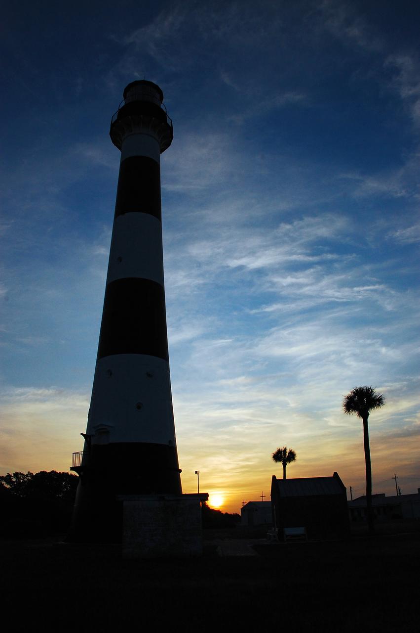 Cape Canaveral Air Force Station, Fla. -- As the sun rises, the Cape Canaveral Lighthouse is silhouetted against the early morning sky. The Canaveral light is the only operating lighthouse owned by the U.S. Air Force. In 2000, the Coast Guard transferred ownership of the lighthouse structure and its grounds to the Air Force, which is now responsible for maintaining it. The U.S. Coast Guard continues to operate the modern first-order beacon as an active navigational aid. The first lighthouse at Cape Canaveral was built near the tip of the Cape in 1848. The structure was only about 60 feet high with a rather dim light powered by whale oil. In 1859, work began nearby on a new, taller iron structure. Construction was halted during the Civil War, and the lighthouse finally was finished in 1868. The structure, with a brick lining inside its iron exterior, was painted with its "daymark" black and white horizontal bands in 1873 to make it easier to identify during the day as a navigation point. Between 1892 and 1894, the lighthouse was dismantled and moved to its new home about a mile from the coast, where it stands today. Photo credit: NASA/Ben Smegelsky