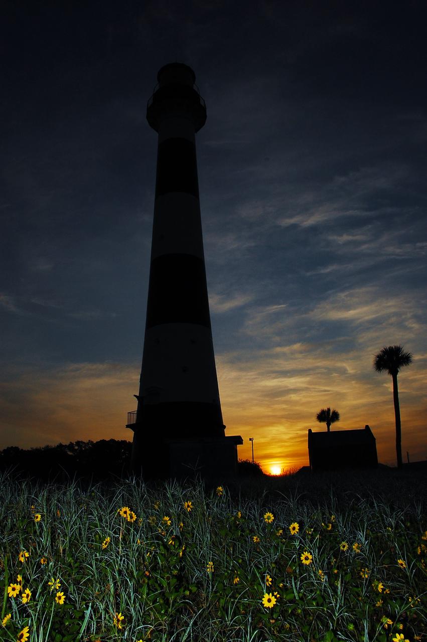 Cape Canaveral Air Force Station, Fla. -- As the sun rises, the Cape Canaveral Lighthouse is silhouetted against the early morning sky. The Canaveral light is the only operating lighthouse owned by the U.S. Air Force. In 2000, the Coast Guard transferred ownership of the lighthouse structure and its grounds to the Air Force, which is now responsible for maintaining it. The U.S. Coast Guard continues to operate the modern first-order beacon as an active navigational aid. The first lighthouse at Cape Canaveral was built near the tip of the Cape in 1848. The structure was only about 60 feet high with a rather dim light powered by whale oil. In 1859, work began nearby on a new, taller iron structure. Construction was halted during the Civil War, and the lighthouse finally was finished in 1868. The structure, with a brick lining inside its iron exterior, was painted with its "daymark" black and white horizontal bands in 1873 to make it easier to identify during the day as a navigation point. Between 1892 and 1894, the lighthouse was dismantled and moved to its new home about a mile from the coast, where it stands today. Photo credit: NASA/Ben Smegelsky