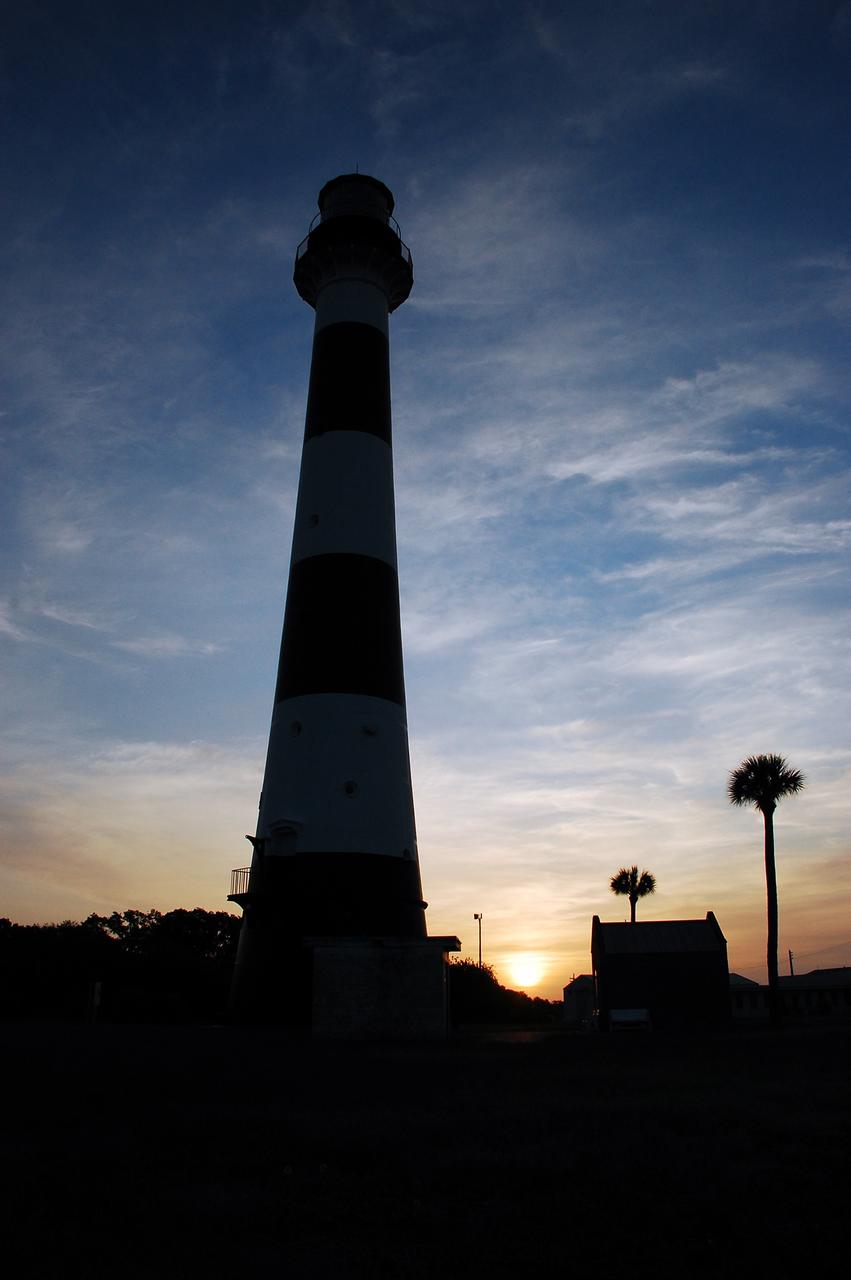 Cape Canaveral Air Force Station, Fla. -- As the sun rises, the Cape Canaveral Lighthouse is silhouetted against the early morning sky. The Canaveral light is the only operating lighthouse owned by the U.S. Air Force. In 2000, the Coast Guard transferred ownership of the lighthouse structure and its grounds to the Air Force, which is now responsible for maintaining it. The U.S. Coast Guard continues to operate the modern first-order beacon as an active navigational aid. The first lighthouse at Cape Canaveral was built near the tip of the Cape in 1848. The structure was only about 60 feet high with a rather dim light powered by whale oil. In 1859, work began nearby on a new, taller iron structure. Construction was halted during the Civil War, and the lighthouse finally was finished in 1868. The structure, with a brick lining inside its iron exterior, was painted with its "daymark" black and white horizontal bands in 1873 to make it easier to identify during the day as a navigation point. Between 1892 and 1894, the lighthouse was dismantled and moved to its new home about a mile from the coast, where it stands today. Photo credit: NASA/Ben Smegelsky