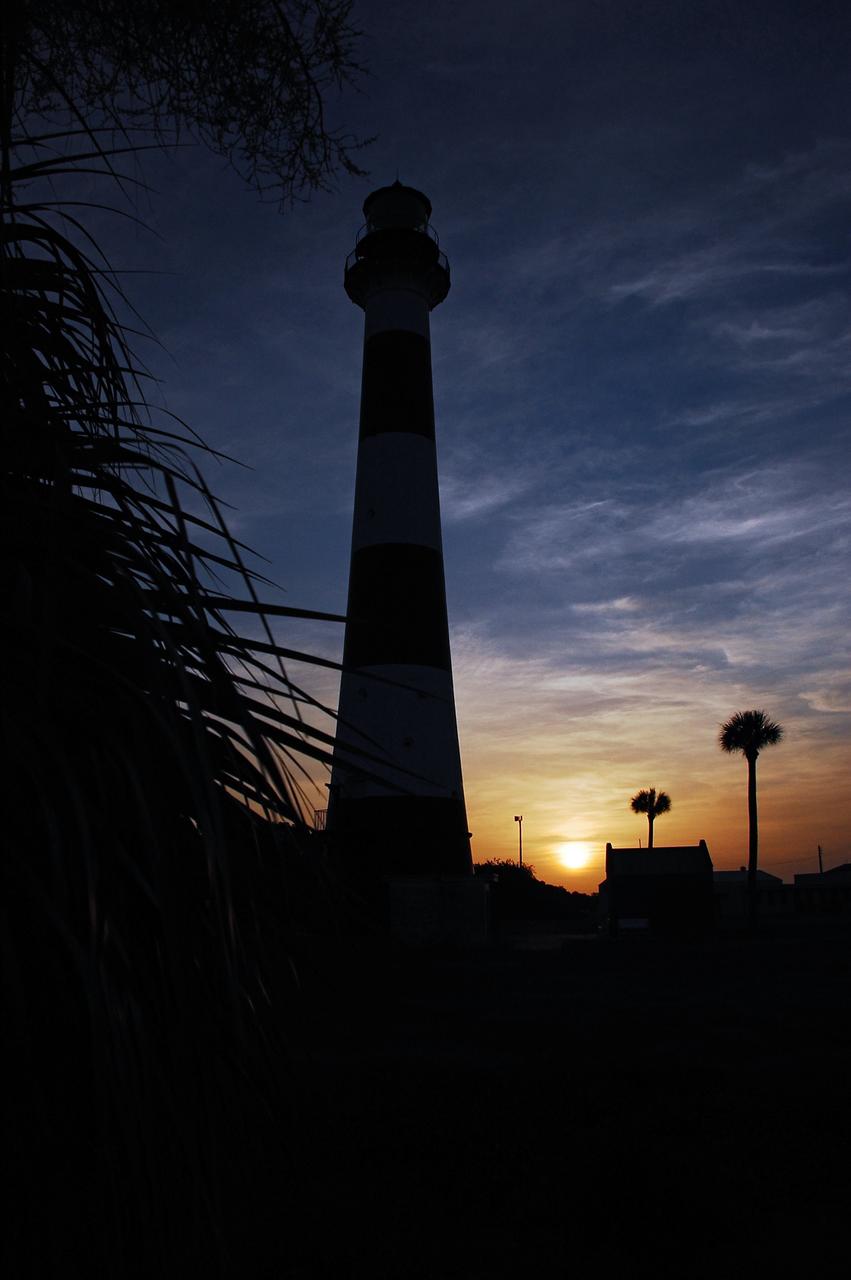 Cape Canaveral Air Force Station, Fla. -- As the sun rises, the Cape Canaveral Lighthouse is silhouetted against the early morning sky. The Canaveral light is the only operating lighthouse owned by the U.S. Air Force. In 2000, the Coast Guard transferred ownership of the lighthouse structure and its grounds to the Air Force, which is now responsible for maintaining it. The U.S. Coast Guard continues to operate the modern first-order beacon as an active navigational aid. The first lighthouse at Cape Canaveral was built near the tip of the Cape in 1848. The structure was only about 60 feet high with a rather dim light powered by whale oil. In 1859, work began nearby on a new, taller iron structure. Construction was halted during the Civil War, and the lighthouse finally was finished in 1868. The structure, with a brick lining inside its iron exterior, was painted with its "daymark" black and white horizontal bands in 1873 to make it easier to identify during the day as a navigation point. Between 1892 and 1894, the lighthouse was dismantled and moved to its new home about a mile from the coast, where it stands today. Photo credit: NASA/Ben Smegelsky