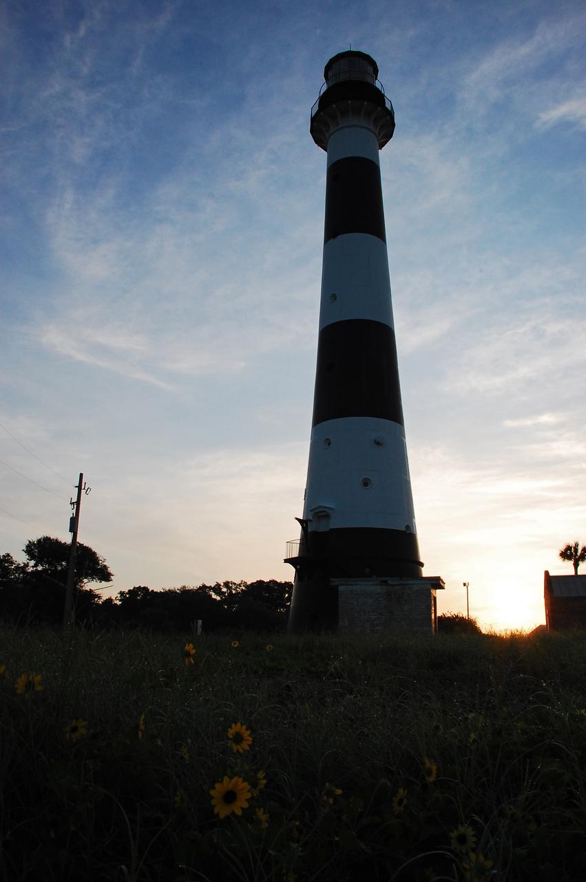 Cape Canaveral Air Force Station, Fla. -- As the sun rises, the Cape Canaveral Lighthouse is silhouetted against the early morning sky. The Canaveral light is the only operating lighthouse owned by the U.S. Air Force. In 2000, the Coast Guard transferred ownership of the lighthouse structure and its grounds to the Air Force, which is now responsible for maintaining it. The U.S. Coast Guard continues to operate the modern first-order beacon as an active navigational aid. The first lighthouse at Cape Canaveral was built near the tip of the Cape in 1848. The structure was only about 60 feet high with a rather dim light powered by whale oil. In 1859, work began nearby on a new, taller iron structure. Construction was halted during the Civil War, and the lighthouse finally was finished in 1868. The structure, with a brick lining inside its iron exterior, was painted with its "daymark" black and white horizontal bands in 1873 to make it easier to identify during the day as a navigation point. Between 1892 and 1894, the lighthouse was dismantled and moved to its new home about a mile from the coast, where it stands today. Photo credit: NASA/Ben Smegelsky