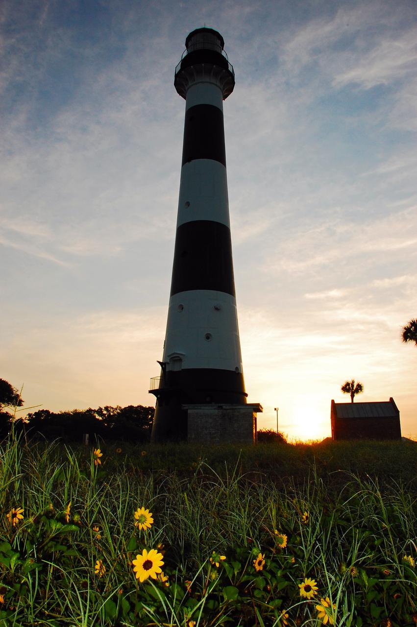 Cape Canaveral Air Force Station, Fla. -- As the sun rises, the Cape Canaveral Lighthouse is silhouetted against the early morning sky. The Canaveral light is the only operating lighthouse owned by the U.S. Air Force. In 2000, the Coast Guard transferred ownership of the lighthouse structure and its grounds to the Air Force, which is now responsible for maintaining it. The U.S. Coast Guard continues to operate the modern first-order beacon as an active navigational aid. The first lighthouse at Cape Canaveral was built near the tip of the Cape in 1848. The structure was only about 60 feet high with a rather dim light powered by whale oil. In 1859, work began nearby on a new, taller iron structure. Construction was halted during the Civil War, and the lighthouse finally was finished in 1868. The structure, with a brick lining inside its iron exterior, was painted with its "daymark" black and white horizontal bands in 1873 to make it easier to identify during the day as a navigation point. Between 1892 and 1894, the lighthouse was dismantled and moved to its new home about a mile from the coast, where it stands today. Photo credit: NASA/Ben Smegelsky