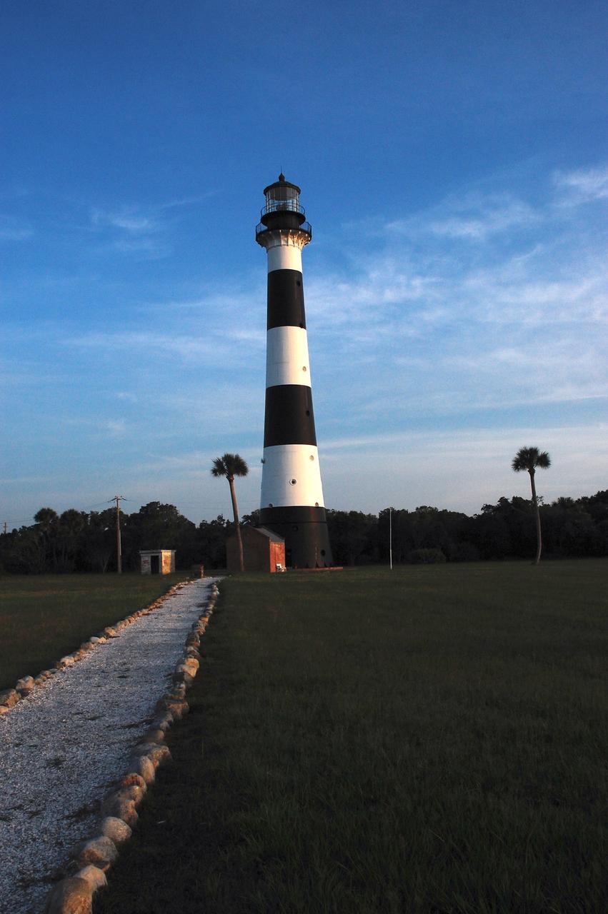 Cape Canaveral Air Force Station, Fla. -- A warm glow envelopes the Cape Canaveral Lighthouse as dawn breaks over the Cape.. The Canaveral light is the only operating lighthouse owned by the U.S. Air Force. In 2000, the Coast Guard transferred ownership of the lighthouse structure and its grounds to the Air Force, which is now responsible for maintaining it. The U.S. Coast Guard continues to operate the modern first-order beacon as an active navigational aid. The first lighthouse at Cape Canaveral was built near the tip of the Cape in 1848. The structure was only about 60 feet high with a rather dim light powered by whale oil. In 1859, work began nearby on a new, taller iron structure. Construction was halted during the Civil War, and the lighthouse finally was finished in 1868. The structure, with a brick lining inside its iron exterior, was painted with its "daymark" black and white horizontal bands in 1873 to make it easier to identify during the day as a navigation point. Between 1892 and 1894, the lighthouse was dismantled and moved to its new home about a mile from the coast, where it stands today. Photo credit: NASA/Ben Smegelsky