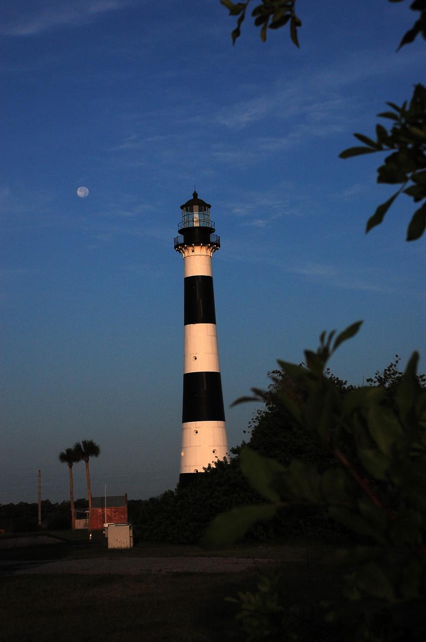 Cape Canaveral Air Force Station, Fla. -- A warm glow envelopes the Cape Canaveral Lighthouse as dawn breaks and a full moon still shines overhead. The Canaveral light is the only operating lighthouse owned by the U.S. Air Force. In 2000, the Coast Guard transferred ownership of the lighthouse structure and its grounds to the Air Force, which is now responsible for maintaining it. The U.S. Coast Guard continues to operate the modern first-order beacon as an active navigational aid. The first lighthouse at Cape Canaveral was built near the tip of the Cape in 1848. The structure was only about 60 feet high with a rather dim light powered by whale oil. In 1859, work began nearby on a new, taller iron structure. Construction was halted during the Civil War, and the lighthouse finally was finished in 1868. The structure, with a brick lining inside its iron exterior, was painted with its "daymark" black and white horizontal bands in 1873 to make it easier to identify during the day as a navigation point. Between 1892 and 1894, the lighthouse was dismantled and moved to its new home about a mile from the coast, where it stands today. Photo credit: NASA/Ben Smegelsky