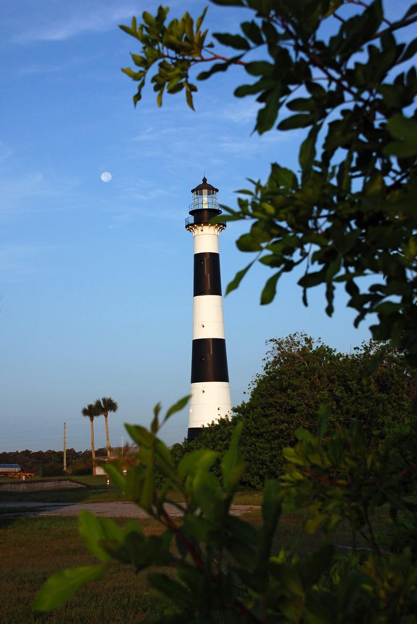 Cape Canaveral Air Force Station, Fla. -- A warm glow envelopes the Cape Canaveral Lighthouse as dawn breaks and a full moon still shines overhead. The Canaveral light is the only operating lighthouse owned by the U.S. Air Force. In 2000, the Coast Guard transferred ownership of the lighthouse structure and its grounds to the Air Force, which is now responsible for maintaining it. The U.S. Coast Guard continues to operate the modern first-order beacon as an active navigational aid. The first lighthouse at Cape Canaveral was built near the tip of the Cape in 1848. The structure was only about 60 feet high with a rather dim light powered by whale oil. In 1859, work began nearby on a new, taller iron structure. Construction was halted during the Civil War, and the lighthouse finally was finished in 1868. The structure, with a brick lining inside its iron exterior, was painted with its "daymark" black and white horizontal bands in 1873 to make it easier to identify during the day as a navigation point. Between 1892 and 1894, the lighthouse was dismantled and moved to its new home about a mile from the coast, where it stands today. Photo credit: NASA/Ben Smegelsky