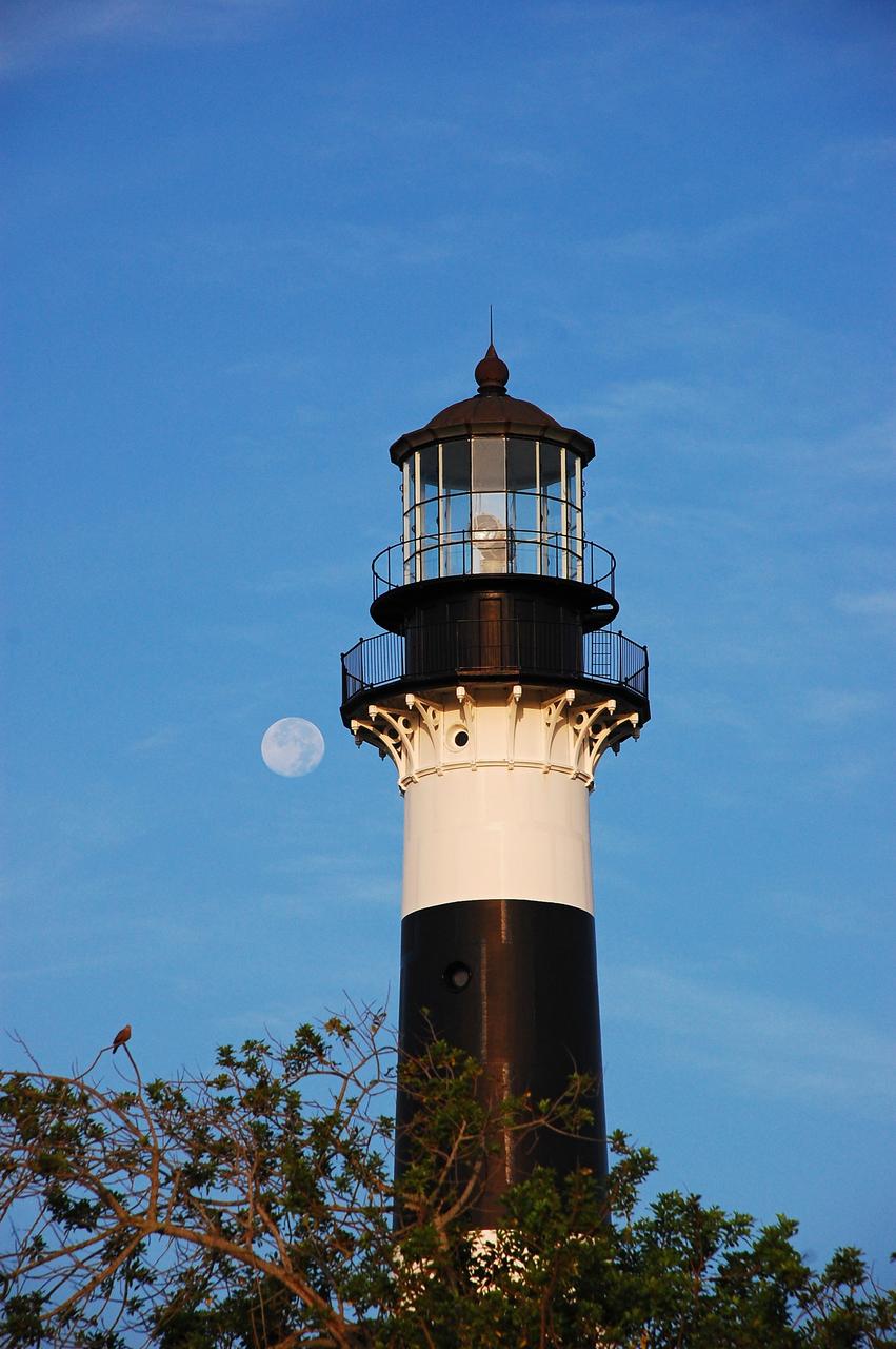 Cape Canaveral Air Force Station, Fla. -- The lantern room of the Cape Canaveral Lighthouse, with its modern first-order optic, takes on a warm glow as dawn breaks and a full moon still shines overhead. The Canaveral light is the only operating lighthouse owned by the U.S. Air Force. In 2000, the Coast Guard transferred ownership of the lighthouse structure and its grounds to the Air Force, which is now responsible for maintaining it. The U.S. Coast Guard continues to operate the beacon as an active navigational aid. The first lighthouse at Cape Canaveral was built near the tip of the Cape in 1848. The structure was only about 60 feet high with a rather dim light powered by whale oil. In 1859, work began nearby on a new, taller iron structure. Construction was halted during the Civil War, and the lighthouse finally was finished in 1868. The structure, with a brick lining inside its iron exterior, was painted with its "daymark" black and white horizontal bands in 1873 to make it easier to identify during the day as a navigation point. Between 1892 and 1894, the lighthouse was dismantled and moved to its new home about a mile from the coast, where it stands today. Photo credit: NASA/Ben Smegelsky