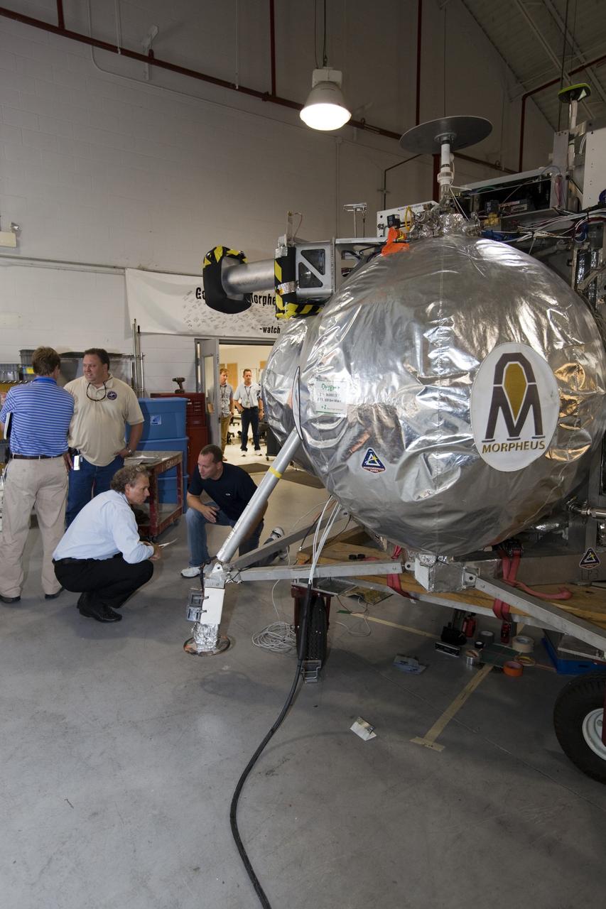 CAPE CANAVERAL, Fla. - Russell Romanella, director of Safety and Mission Assurance at NASA's Kennedy Space Center in Florida, kneeling on the left, is briefed on NASA's Morpheus lander, a vertical test bed vehicle. Morpheus is being checked out by technicians and engineers in a building at the Shuttle Landing Facility, or SLF, at Kennedy. Morpheus is designed to demonstrate new green propellant propulsion systems and autonomous landing and an Autonomous Landing and Hazard Avoidance Technology, or ALHAT, system. Checkout of the prototype lander has been ongoing at NASA’s Johnson Space Center in Houston in preparation for its first free flight. The SLF site will provide the lander with the kind of field necessary for realistic testing. Project Morpheus is one of 20 small projects comprising the Advanced Exploration Systems, or AES, program in NASA’s Human Exploration and Operations Mission Directorate. AES projects pioneer new approaches for rapidly developing prototype systems, demonstrating key capabilities and validating operational concepts for future human missions beyond Earth orbit. For more information on Project Morpheus, visit http://www.nasa.gov/centers/johnson/exploration/morpheus/index.html Photo credit: NASA/Dimitri Gerondidakis