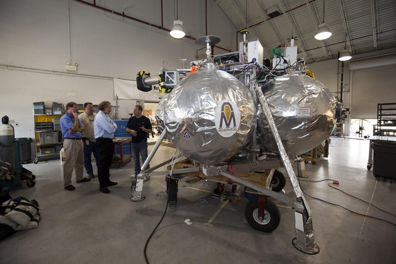 CAPE CANAVERAL, Fla. - Russell Romanella, director of Safety and Mission Assurance at NASA's Kennedy Space Center in Florida, right-center, is briefed on NASA's Morpheus lander, a vertical test bed vehicle. Morpheus is being checked out by technicians and engineers in a building at the Shuttle Landing Facility, or SLF, at Kennedy. Morpheus is designed to demonstrate new green propellant propulsion systems and autonomous landing and an Autonomous Landing and Hazard Avoidance Technology, or ALHAT, system.      Checkout of the prototype lander has been ongoing at NASA’s Johnson Space Center in Houston in preparation for its first free flight. The SLF site will provide the lander with the kind of field necessary for realistic testing. Project Morpheus is one of 20 small projects comprising the Advanced Exploration Systems, or AES, program in NASA’s Human Exploration and Operations Mission Directorate. AES projects pioneer new approaches for rapidly developing prototype systems, demonstrating key capabilities and validating operational concepts for future human missions beyond Earth orbit. For more information on Project Morpheus, visit http://www.nasa.gov/centers/johnson/exploration/morpheus/index.html  Photo credit: NASA/Dimitri Gerondidakis