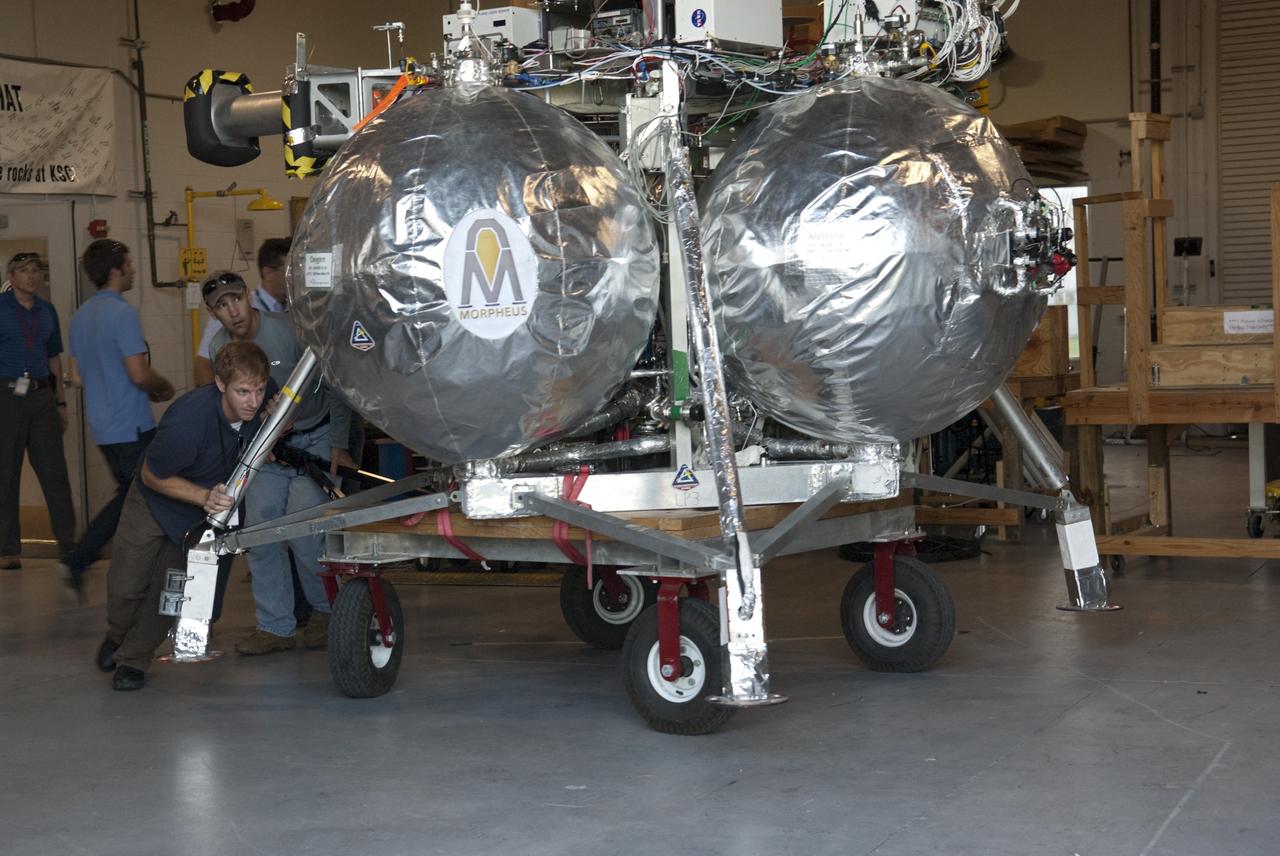 CAPE CANAVERAL, Fla. - NASA's Morpheus lander, a vertical test bed vehicle, is being moved out of its checkout building for a short trip to a launch position at the Shuttle Landing Facility, or SLF, at the Kennedy Space Center in Florida. Morpheus is designed to demonstrate new green propellant propulsion systems and autonomous landing and an Autonomous Landing and Hazard Avoidance Technology, or ALHAT, system. Checkout of the prototype lander has been ongoing at NASA’s Johnson Space Center in Houston in preparation for its first free flight. The SLF site will provide the lander with the kind of field necessary for realistic testing. Project Morpheus is one of 20 small projects comprising the Advanced Exploration Systems, or AES, program in NASA’s Human Exploration and Operations Mission Directorate. AES projects pioneer new approaches for rapidly developing prototype systems, demonstrating key capabilities and validating operational concepts for future human missions beyond Earth orbit. For more information on Project Morpheus, visit http://www.nasa.gov/centers/johnson/exploration/morpheus/index.html Photo credit: NASA/Dimitri Gerondidakis