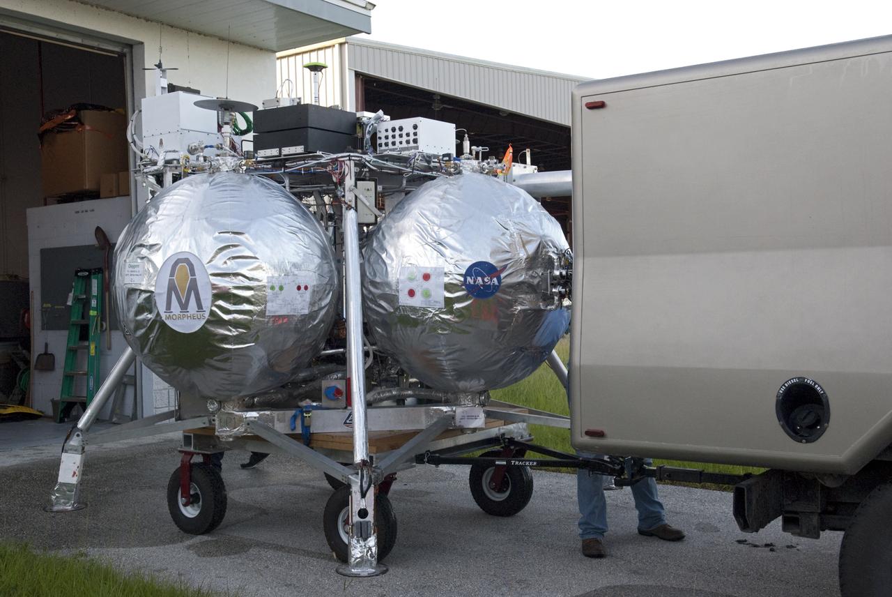 CAPE CANAVERAL, Fla. - NASA's Morpheus lander, a vertical test bed vehicle, is being transported out of its checkout building for a short trip to a launch position at the Shuttle Landing Facility, or SLF, at the Kennedy Space Center in Florida. Morpheus is designed to demonstrate new green propellant propulsion systems and autonomous landing and an Autonomous Landing and Hazard Avoidance Technology, or ALHAT, system. Checkout of the prototype lander has been ongoing at NASA’s Johnson Space Center in Houston in preparation for its first free flight. The SLF site will provide the lander with the kind of field necessary for realistic testing. Project Morpheus is one of 20 small projects comprising the Advanced Exploration Systems, or AES, program in NASA’s Human Exploration and Operations Mission Directorate. AES projects pioneer new approaches for rapidly developing prototype systems, demonstrating key capabilities and validating operational concepts for future human missions beyond Earth orbit. For more information on Project Morpheus, visit http://www.nasa.gov/centers/johnson/exploration/morpheus/index.html Photo credit: NASA/Dimitri Gerondidakis