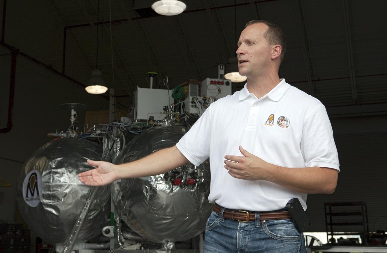 CAPE CANAVERAL, Fla. - At a hangar near the Shuttle Landing Facility, or SLF, at NASA’s Kennedy Space Center in Florida, the Johnson Space Center Project Morpheus Manager Jon Olansen speaks to members of the media. In the background is the Morpheus prototype lander, which arrived at Kennedy on July 27. Testing of the prototype lander had been ongoing at NASA’s Johnson Space Center in Houston in preparation for its first free-flight test at Kennedy Space Center. The SLF will provide the lander with the kind of field necessary for realistic testing, complete with rocks, craters and hazards to avoid. Morpheus utilizes an autonomous landing and hazard avoidance technology, or ALHAT, payload that will allow it to navigate to clear landing sites amidst rocks, craters and other hazards during its descent. Project Morpheus is one of 20 small projects comprising the Advanced Exploration Systems, or AES, program in NASA’s Human Exploration and Operations Mission Directorate. AES projects pioneer new approaches for rapidly developing prototype systems, demonstrating key capabilities and validating operational concepts for future human missions beyond Earth orbit. For more information on Project Morpheus, visit http://morpheuslander.jsc.nasa.gov/. Photo credit: NASA/Kim Shiflett