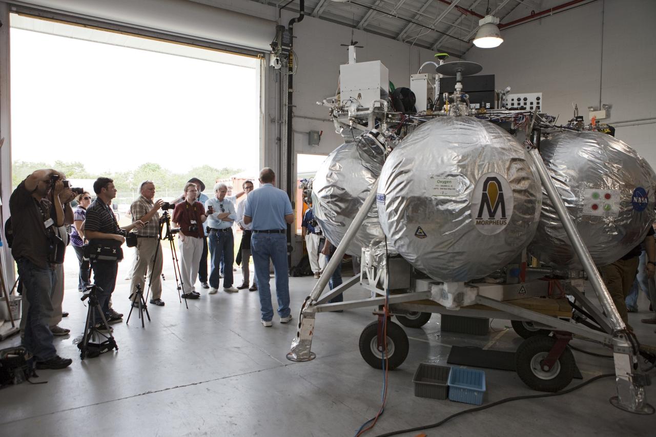 CAPE CANAVERAL, Fla. - At a hangar near the Shuttle Landing Facility, or SLF, at NASA’s Kennedy Space Center in Florida, Chirold Epp, Johnson Space Center Project Manager for ALHAT, speaks to members of the media. In the background is the Morpheus prototype lander, which arrived at Kennedy on July 27. Testing of the prototype lander had been ongoing at NASA’s Johnson Space Center in Houston in preparation for its first free-flight test at Kennedy Space Center. The SLF will provide the lander with the kind of field necessary for realistic testing, complete with rocks, craters and hazards to avoid. Morpheus utilizes an autonomous landing and hazard avoidance technology, or ALHAT, payload that will allow it to navigate to clear landing sites amidst rocks, craters and other hazards during its descent. Project Morpheus is one of 20 small projects comprising the Advanced Exploration Systems, or AES, program in NASA’s Human Exploration and Operations Mission Directorate. AES projects pioneer new approaches for rapidly developing prototype systems, demonstrating key capabilities and validating operational concepts for future human missions beyond Earth orbit. For more information on Project Morpheus, visit http://morpheuslander.jsc.nasa.gov/. Photo credit: NASA/Kim Shiflett