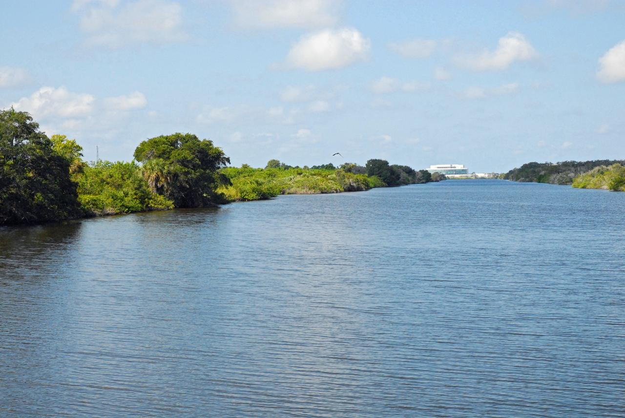CAPE CANAVERAL, Fla. – Operations Support Building II, or OSBII, is seen in the distance during a field-guided boat tour of NASA's Kennedy Space Center in Florida. As part of the center's first-ever Innovation Expo, the tour, called "Living Outdoor Laboratory for Environmental Sustainability," is giving employees the opportunity to see the unique estuarine ecosystems that are protected from development by the presence of Kennedy and the Merritt Island National Wildlife Refuge.     The diverse and healthy area encompassing about 140,000 acres of central Florida's east coast has been closed to the public for 50 years, allowing the coastal dunes, saltwater estuaries and marshes, freshwater impoundments, scrub, pine flatwoods, and hardwood hammocks to provide habitats for more than 1,000 species of plants and animals. Innovation Expo is showcasing the innovative work taking place throughout the center's facilities and labs to encourage employees to work together to solve future challenges. For more information, visit http://www.nasa.gov/kennedy. Photo credit: NASA