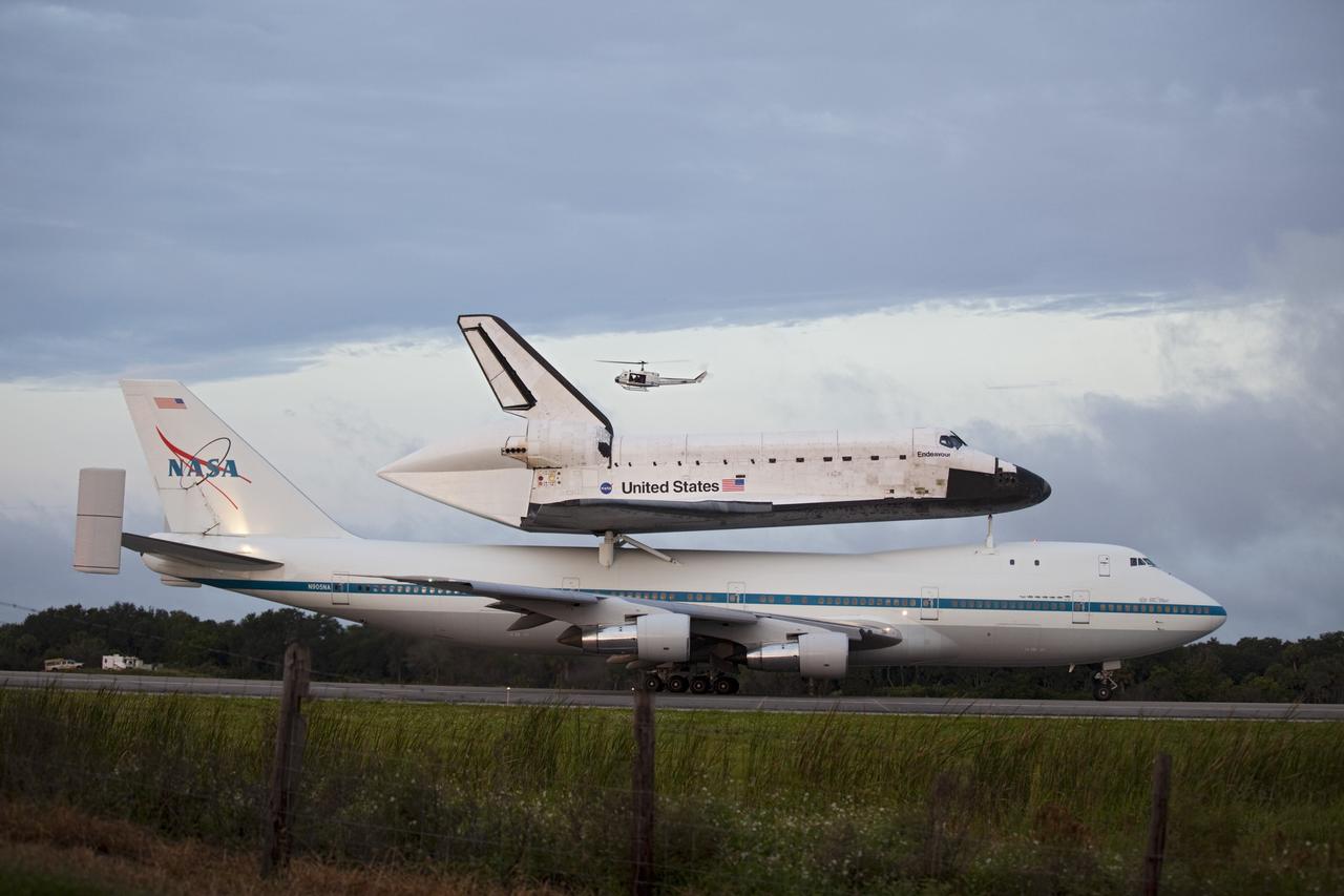 CAPE CANAVERAL, Fla. – At the Shuttle Landing Facility at NASA's Kennedy Space Center in Florida, the crew of a helicopter watch as NASA's Shuttle Carrier Aircraft, or SCA, with the space shuttle Endeavour mounted atop, taxis on the runway for its ferry flight to California. The SCA, a modified 747 jetliner, will fly Endeavour to Los Angeles where it will be placed on public display at the California Science Center. This is the final ferry flight scheduled in the Space Shuttle Program era. For more information on the shuttles' transition and retirement, visit http://www.nasa.gov/transition. Photo credit: NASA/Frankie Martin