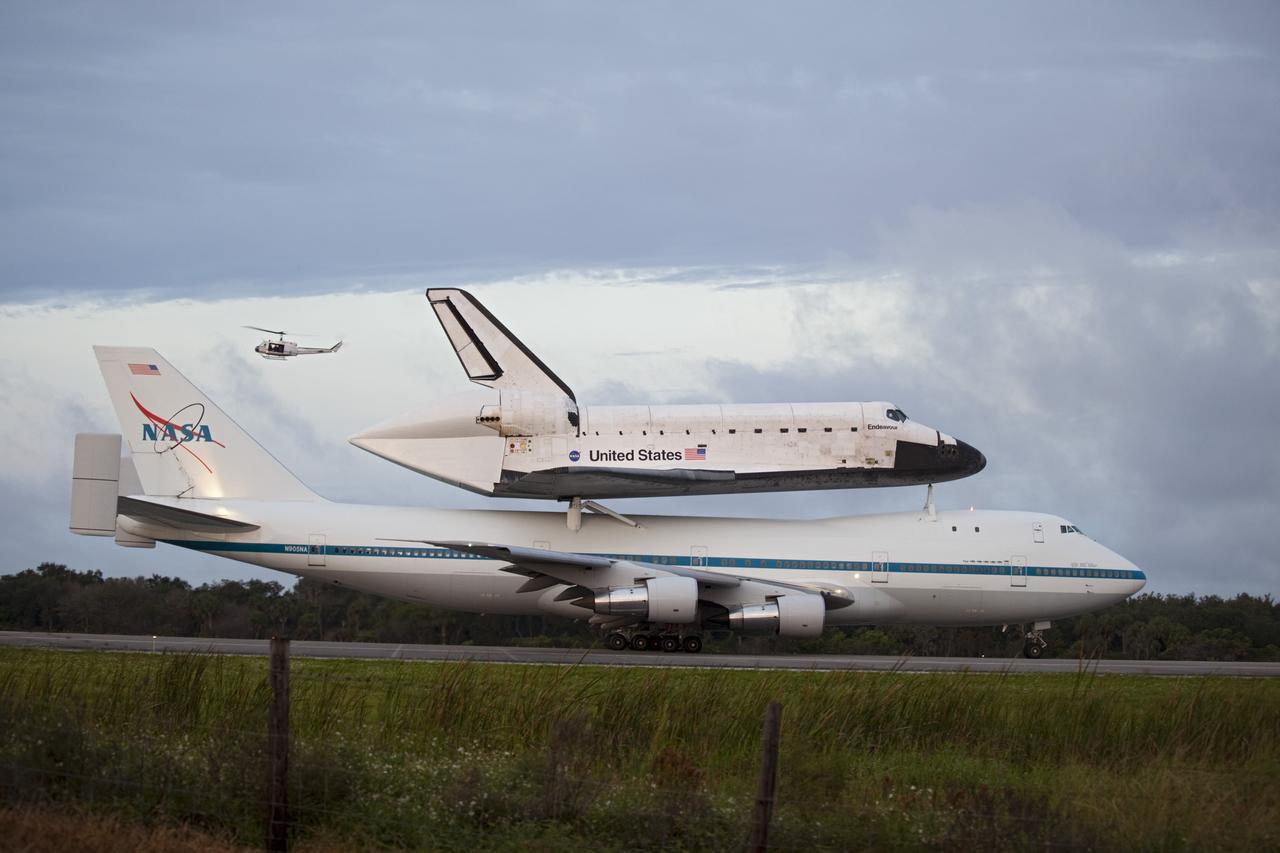 CAPE CANAVERAL, Fla. – At the Shuttle Landing Facility at NASA's Kennedy Space Center in Florida, the crew of a helicopter watch as NASA's Shuttle Carrier Aircraft, or SCA, with the space shuttle Endeavour mounted atop, taxis on the runway for its ferry flight to California. The SCA, a modified 747 jetliner, will fly Endeavour to Los Angeles where it will be placed on public display at the California Science Center. This is the final ferry flight scheduled in the Space Shuttle Program era. For more information on the shuttles' transition and retirement, visit http://www.nasa.gov/transition. Photo credit: NASA/Frankie Martin