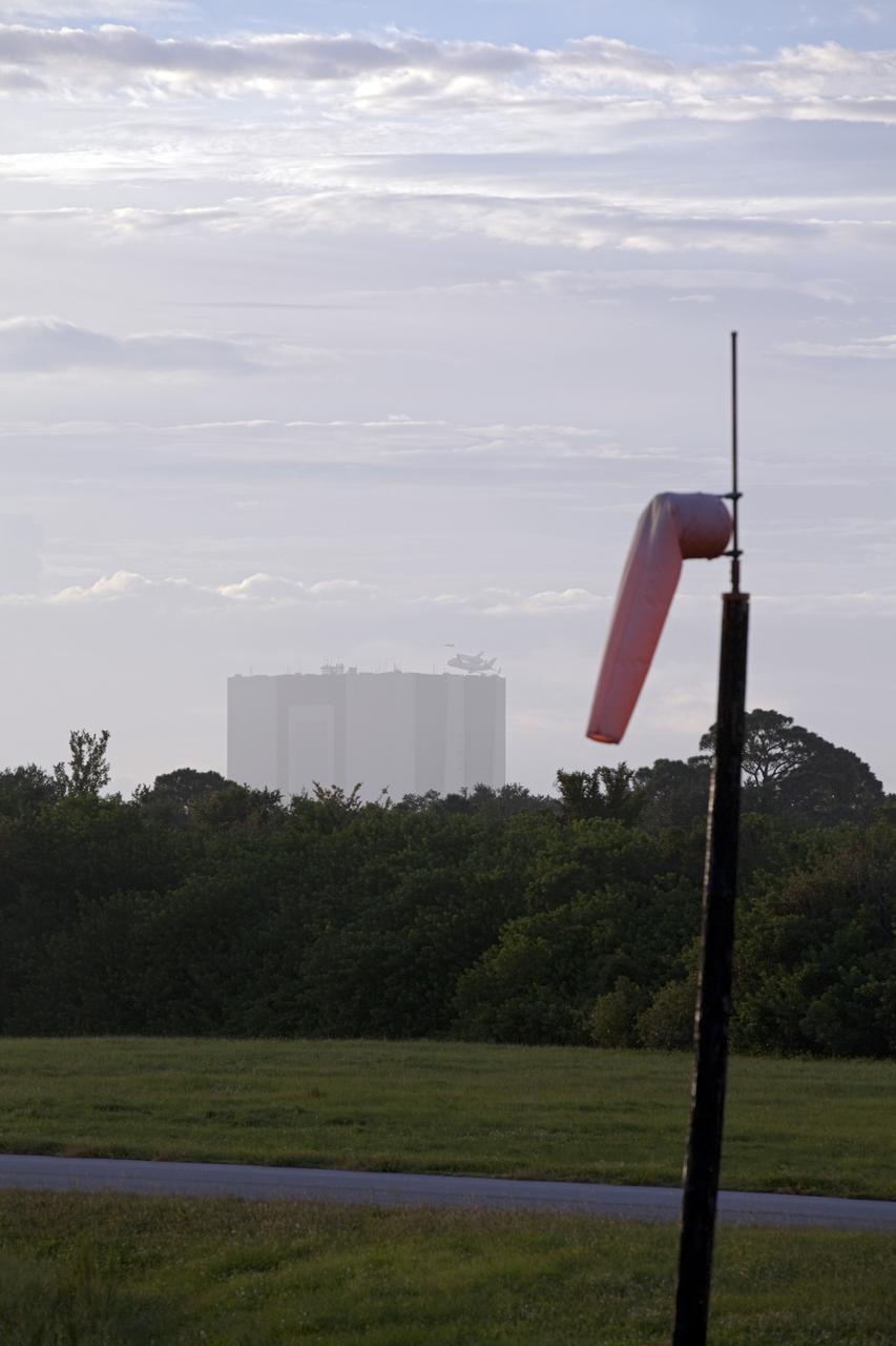 CAPE CANAVERAL, Fla. – At the Shuttle Landing Facility at NASA's Kennedy Space Center in Florida, NASA's Shuttle Carrier Aircraft, or SCA, with the space shuttle Endeavour mounted atop, flies over the Vehicle Assembly Building after takeoff for its ferry flight to California. A runway wind sock is in the foreground. The SCA, a modified 747 jetliner, will fly Endeavour to Los Angeles where it will be placed on public display at the California Science Center. This is the final ferry flight scheduled in the Space Shuttle Program era. For more information on the shuttles' transition and retirement, visit http://www.nasa.gov/transition. Photo credit: NASA/Frankie Martin