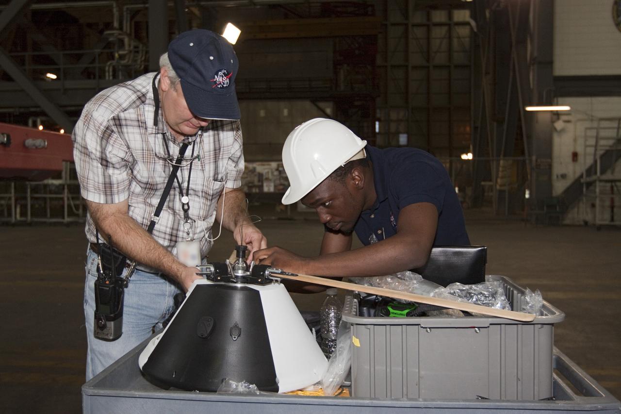 CAPE CANAVERAL, Fla. - NASA's Johnson Space Center Aerospace Engineer Jeff Hagen, left, and engineering intern Emmanuel Nyangweso attach rotors to the top of a model capsule ahead of tests inside the Vehicle Assembly Building at NASA's Kennedy Space Center in Florida. The design would give a capsule the stability and control of a helicopter, but would not be powered. Instead, the wind passing over the rotors as the capsule descends would make the blades turn, a process called auto-rotation. The intent is to give real spacecraft a soft landing with enough control that they could touch down anywhere in the world, whether it be a runway or parking lot. In other words, wherever a helicopter could land, a spacecraft could land, too. Photo credit: NASA/Kim Shiflett
