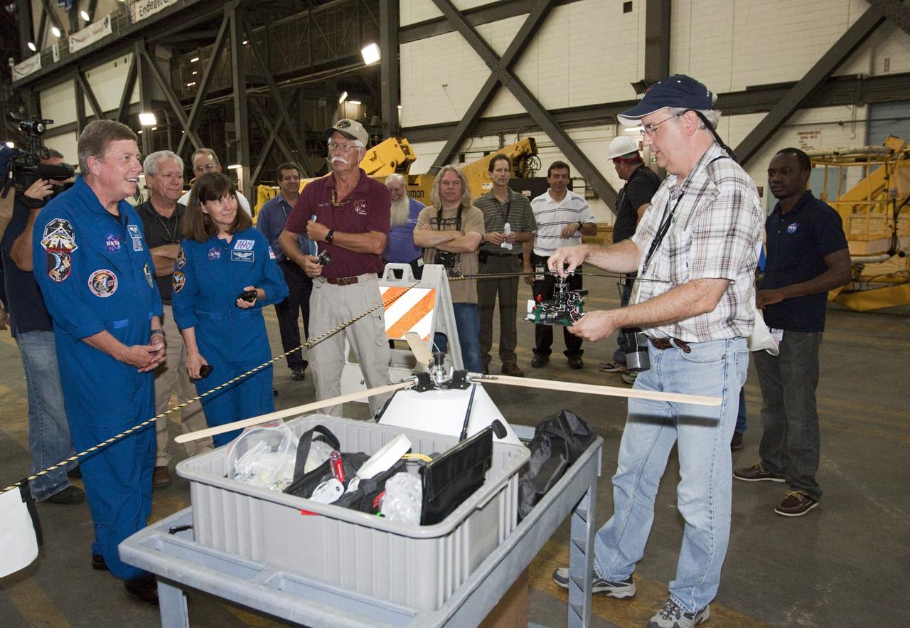 CAPE CANAVERAL, Fla. - Astronauts Mike Fossum and Cady Coleman, both in blue flight suits, listen as NASA's Johnson Space Center Aerospace Engineer Jeff Hagen explains the rotor mechanism for a model capsule ahead of tests inside the Vehicle Assembly Building at NASA's Kennedy Space Center in Florida. The design would give a capsule the stability and control of a helicopter, but would not be powered. Instead, the wind passing over the rotors as the capsule descends would make the blades turn, a process called auto-rotation. The intent is to give real spacecraft a soft landing with enough control that they could touch down anywhere in the world, whether it be a runway or parking lot. In other words, wherever a helicopter could land, a spacecraft could land, too. Photo credit: NASA/Kim Shiflett