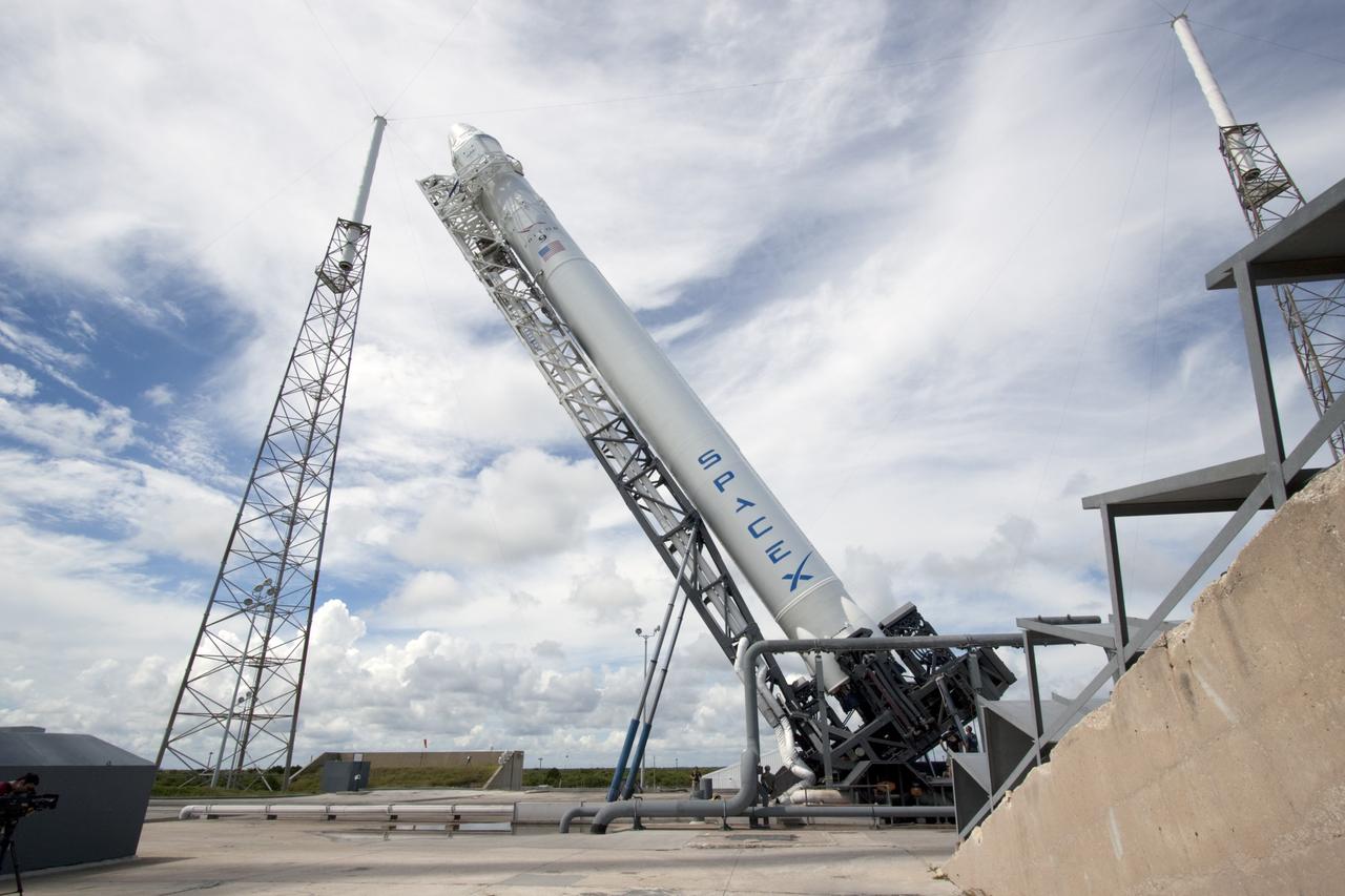 CAPE CANAVERAL, Fla. -- A Falcon 9 rocket with a Dragon capsule secured atop is lifted into a vertical position between the lightning masts on the pad at Space Launch Complex 40 on Cape Canaveral Air Force Station in Florida.     Space Exploration Technologies Corp., or SpaceX, built both the rocket and capsule for NASA's first Commercial Resupply Services, or CRS-1, mission to the International Space Station.  The vertical lift was complete at 1 p.m. EDT.  SpaceX CRS-1 is an important step toward making America’s microgravity research program self-sufficient by providing a way to deliver and return significant amounts of cargo, including science experiments, to and from the orbiting laboratory. Launch is scheduled for 8:35 p.m. EDT on Oct. 7. NASA has contracted for 12 commercial resupply flights from SpaceX and eight from the Orbital Sciences Corp. For more information, visit http://www.nasa.gov/mission_pages/station/living/launch/index.html.  Photo credit: NASA/Jim Grossmann