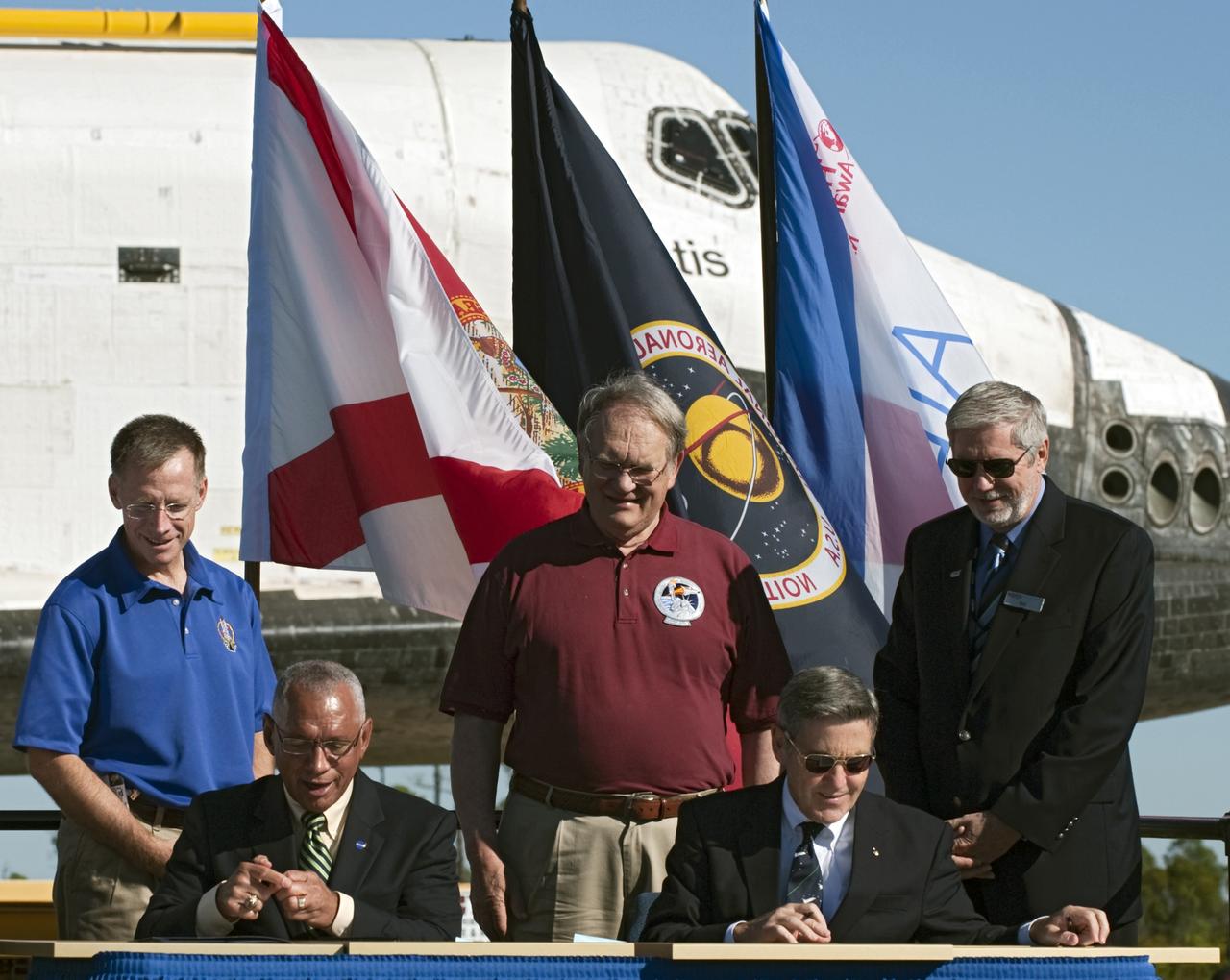 CAPE CANAVERAL, Fla. – At NASA's Kennedy Space Center in Florida, the space shuttle Atlantis pauses during its 10-mile journey to the Kennedy visitor complex for a ceremony to commemorate its transfer. NASA Administrator Charles Bolden, seated left, and Kennedy Director Bob Cabana sign documents transferring title of Atlantis from the agency to Kennedy Space Center. Also participating in the ceremony, standing, from left, are Chris Ferguson, who commanded Atlantis' final mission, Karol Bobko, commander of Atlantis' first mission and Delaware North Companies Parks and Resorts Chief Operating Officer Bill Moore.      As part of transition and retirement of the Space Shuttle Program, Atlantis is to be displayed at Kennedy's Visitor Complex beginning in the summer of 2013. Over the course of its 26-year career, Atlantis traveled 125,935,769 miles during 307 days in space over 33 missions. For more information, visit http://www.nasa.gov/transition Photo credit: NASA/ Tony Gray