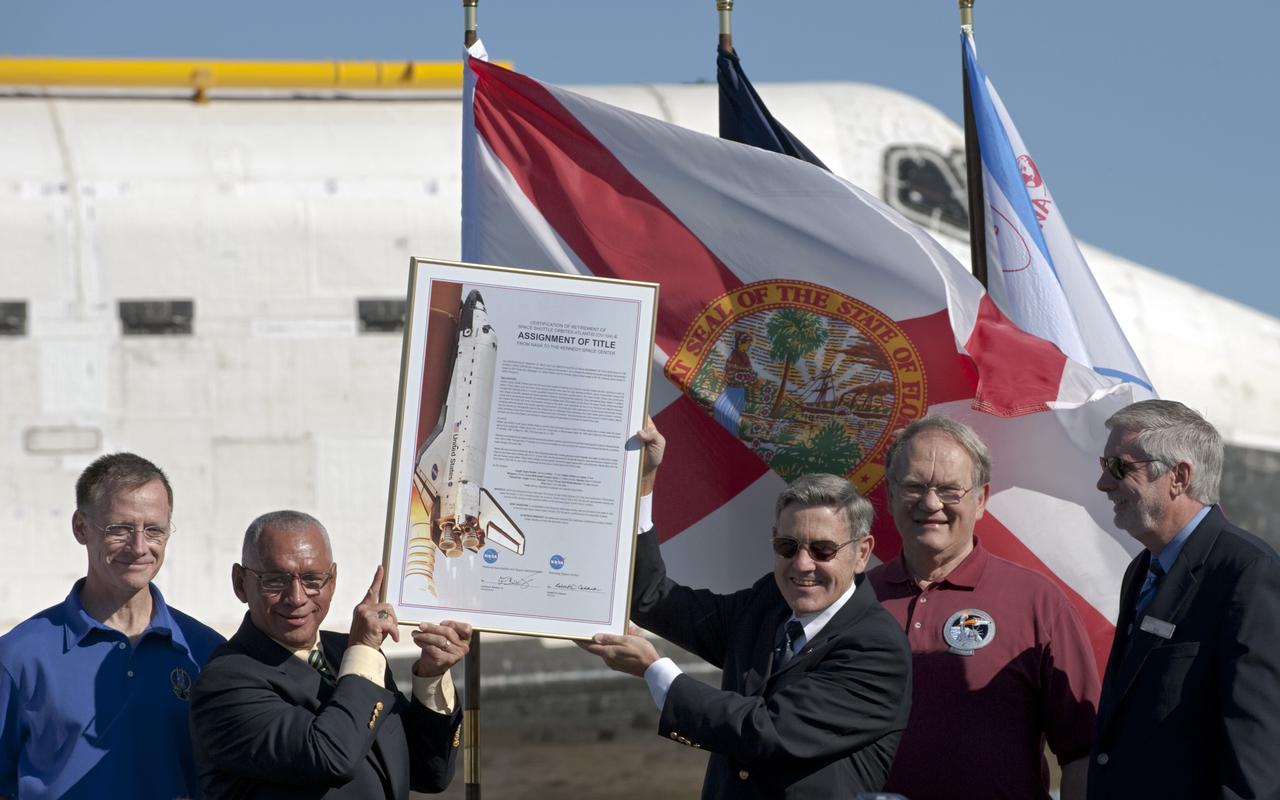 CAPE CANAVERAL, Fla. – At NASA's Kennedy Space Center in Florida, the space shuttle Atlantis pauses during its 10-mile journey to the Kennedy visitor complex for a ceremony to commemorate its transfer. NASA Administrator Charles Bolden, left, and Kennedy Director Bob Cabana hold the just-signed document transferring title of Atlantis from the agency to Kennedy Space Center. Participating in the ceremony, from left, are Chris Ferguson, who commanded Atlantis' final mission, Bolden, Cabana, Karol Bobko, commander of Atlantis' first mission, and Delaware North Companies Parks and Resorts Chief Operating Officer Bill Moore.      As part of transition and retirement of the Space Shuttle Program, Atlantis is to be displayed at Kennedy's visitor complex beginning in the summer of 2013. Over the course of its 26-year career, Atlantis traveled 125,935,769 miles during 307 days in space over 33 missions. For more information, visit http://www.nasa.gov/transition Photo credit: NASA/ Tony Gray