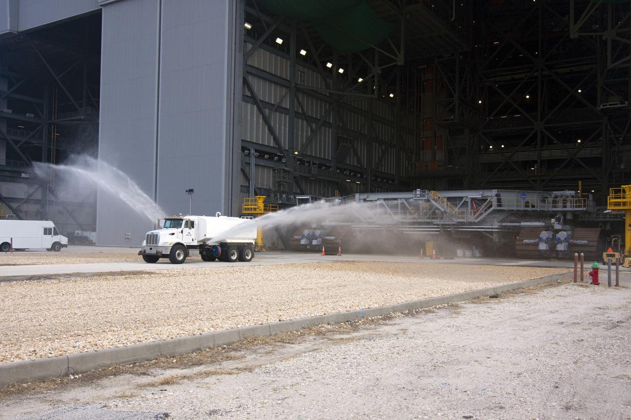 CAPE CANAVERAL, Fla. -- A truck sprays water on the gravel crawler way at NASA's Kennedy Space Center in Florida as crawler-transporter No. 2 moves out of high bay 2 of the Vehicle Assembly Building. With crawler-transporter modifications complete, the test drive is designed to check out modifications to ensure its ability to carry launch vehicles such as the space agency's Space Launch System heavy-lift rocket to the launch pad. NASA's Ground Systems Development and Operations Program is leading the 20-year life-extension project for the crawler. A pair of behemoth machines called crawler-transporters has carried the load of taking rockets and spacecraft to the launch pad for more than 40 years at NASA’s Kennedy Space Center in Florida. Each the size of a baseball infield and powered by locomotive and large electrical power generator engines, the crawler-transporters will stand ready to keep up the work for the next generation of launch vehicles projects to lift astronauts into space. For more information, visit http://www.nasa.gov/exploration/systems/ground/index.html Photo credit: NASA/Jim Grossmann