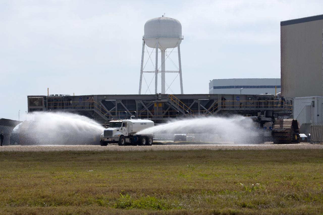 CAPE CANAVERAL, Fla. -- A truck sprays water on the gravel crawler way at NASA's Kennedy Space Center in Florida as crawler-transporter No. 2 moves out of high bay 2 of the Vehicle Assembly Building. With crawler-transporter modifications complete, the test drive is designed to check out modifications to ensure its ability to carry launch vehicles such as the space agency's Space Launch System heavy-lift rocket to the launch pad. NASA's Ground Systems Development and Operations Program is leading the 20-year life-extension project for the crawler. A pair of behemoth machines called crawler-transporters has carried the load of taking rockets and spacecraft to the launch pad for more than 40 years at NASA’s Kennedy Space Center in Florida. Each the size of a baseball infield and powered by locomotive and large electrical power generator engines, the crawler-transporters will stand ready to keep up the work for the next generation of launch vehicles projects to lift astronauts into space. For more information, visit http://www.nasa.gov/exploration/systems/ground/index.html Photo credit: NASA/Jim Grossmann