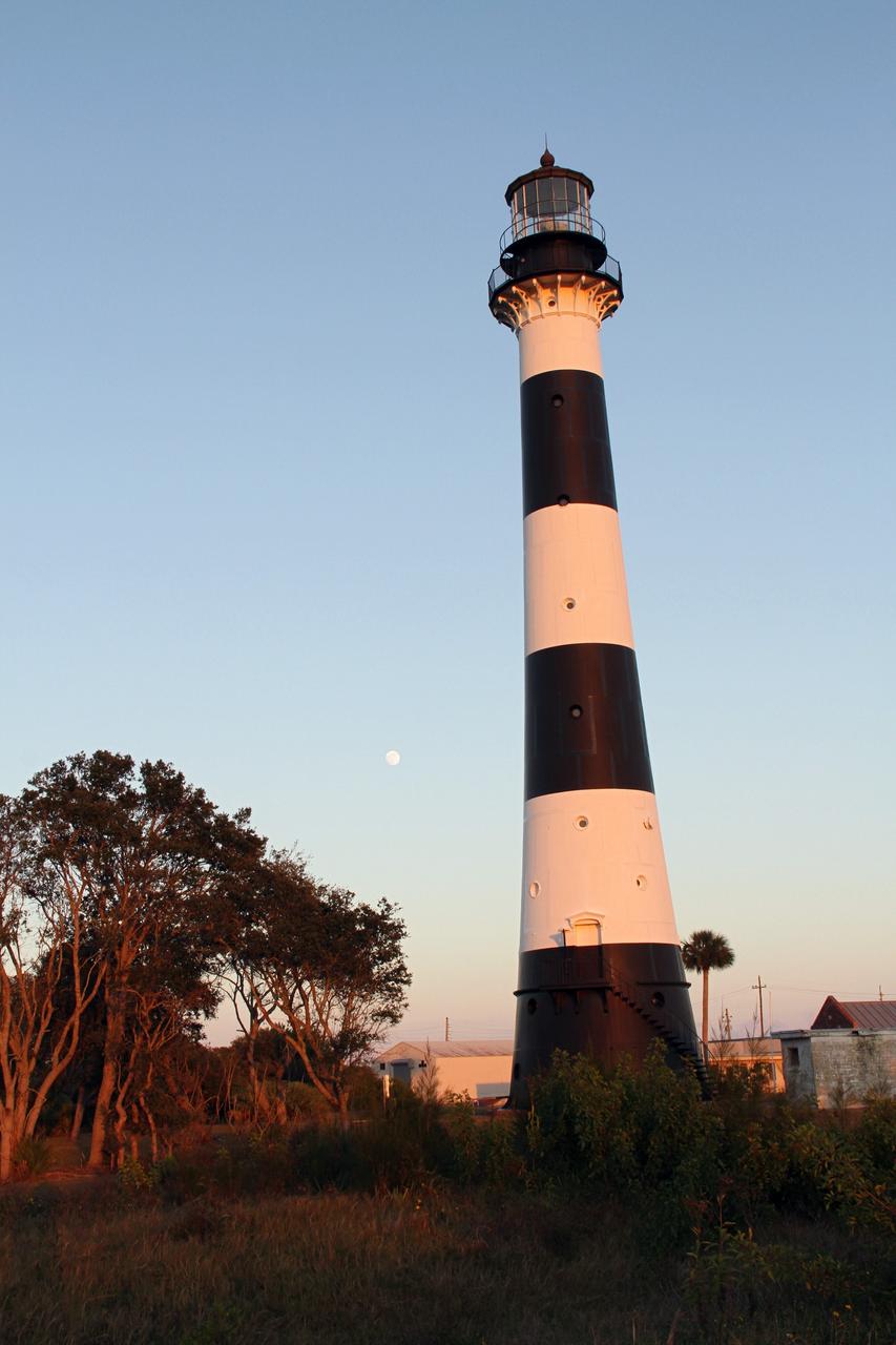 CAPE CANAVERAL AIR FORCE STATION, Fla. – The Cape Canaveral Air Force Station lighthouse takes on a warm glow as dawn breaks and a full moon still shines in the background. The Canaveral light is the only one owned by the U.S. Air Force.      In 2000, the Coast Guard transferred ownership of the lighthouse structure and its grounds to the Air Force, which is now responsible for maintaining it. The U.S. Coast Guard continues to operate the beacon as an active navigational aid. The first lighthouse at Cape Canaveral was built near the tip of the Cape in 1848. The structure was only about 60 feet high with a rather dim light powered by whale oil. In 1859, work began nearby on a new, taller iron structure. Construction was halted during the Civil War, and the lighthouse finally was finished in 1868. The structure, with a brick lining inside its iron exterior, was painted with its "daymark" black and white horizontal bands in 1873 to make it easier to identify during the day as a navigation point. Between 1892 and 1894, the lighthouse was dismantled and moved to its new home about a mile from the coast, where it stands today. Photo credit: NASA/Ben Smegelsky