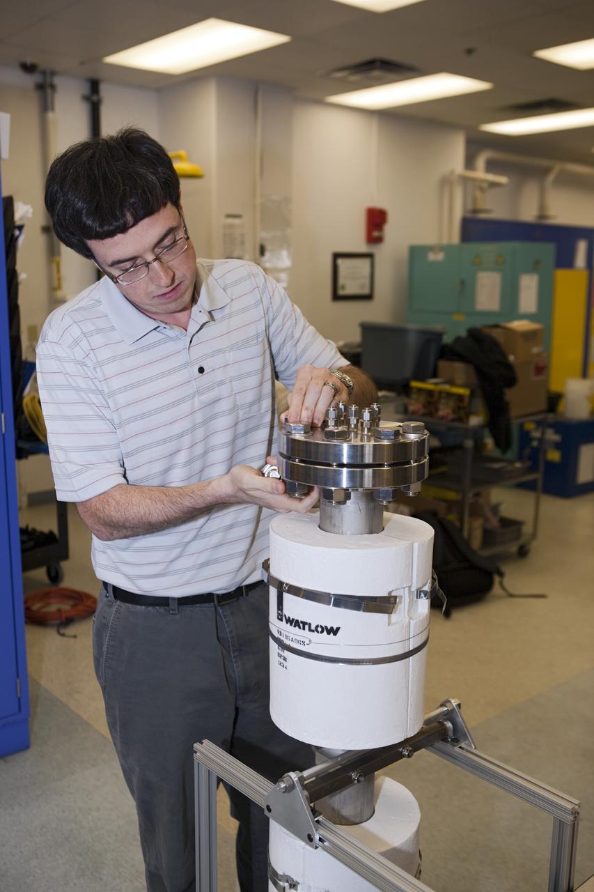 KSC-2012-6320 – CAPE CANAVERAL, Fla. - Stephen Anthony works with an experimental reactor as part of the trash-to-gas project at NASA's Kennedy Space Center in Florida. A group of six researchers at Kennedy and groups from NASA centers in Ohio, California and Texas wrote in a recent paper that the current methods of handling trash – either carrying it along on the round trip through space or gathering it into an expendable module and burning it up in Earth's atmosphere – are not suitable answers for missions that go beyond Earth orbit or even past the moon. Working in a laboratory at Kennedy, Hintze's team built an 80-pound device that looks like a three-foot-long metal pipe to test theories about incinerating a variety of trash ranging from used clothes to uneaten food. The reactor holds more than three quarts of material and burns at about 1,000 degrees F, about twice the maximum temperature of an average household oven. It's expected to take astronauts four hours to burn a day's worth of trash from a crew of four. During the course of a year in space – one half the length of time a mission to Mars is expected to take – trash processing for a crew of four would create about 2,200 pounds of methane fuel, enough to power a launch from the lunar surface, Hintze said. Photo credit: NASA/Dmitri Gerondidakis