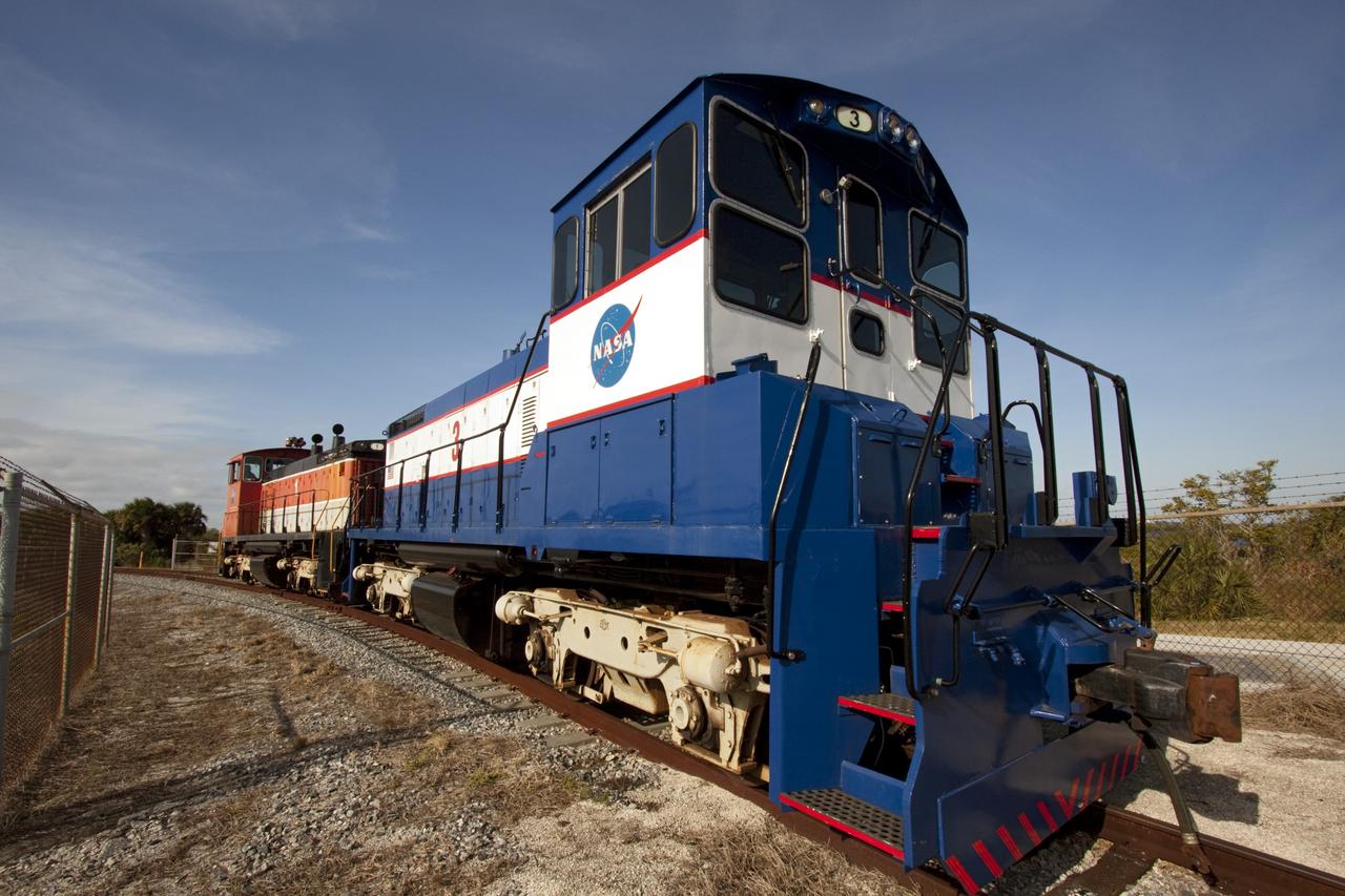 CAPE CANAVERAL, Fla. – NASA locomotive No. 1 pulls locomotive No. 3 out of the Rotation, Processing and Surge Facility, or RPSF, at the Kennedy Space Center in Florida. Inside, an overhead crane was used to lift NASA locomotive No. 2 off of its trucks and moved aside, so locomotive No. 3 could be raised off its trucks and moved into position atop the trucks previously used by locomotive No. 2.       The RPSF was built to support work on the solid rocket used motors during the space shuttle era. The facility had never previously been used for another purpose, but is now free to serve other customers. With rails running into the building's high bay and a pair of heavy-lift cranes positioned overhead, the facility's capabilities were a perfect fit for the NASA Railroad's needs. Railroad managers wanted to trade the wheel and axle assemblies, or trucks, of locomotives No. 2 and No. 3. Locomotive No. 3 was painstakingly restored in recent years by the NASA Railroad team, and handles much of the rail work required at the center in the post-shuttle era. But the trucks on locomotive No. 2 are in better shape and are more environmentally friendly. For more information, visit: http://www.nasa.gov/exploration/systems/ground/rpsf_locomotives.html Photo credit: NASA/Jim Grossmann