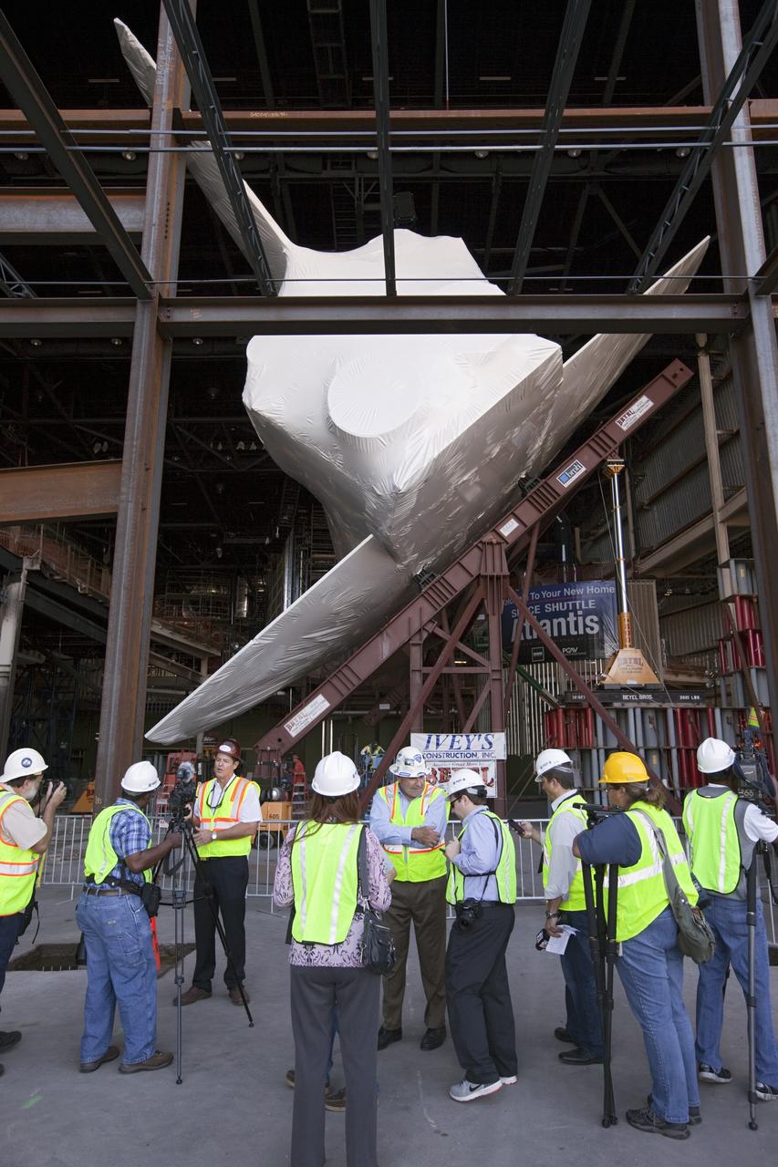 CAPE CANAVERAL, Fla. – Members of the media get an up close view of space shuttle Atlantis in her new home at the Kennedy Space Center Visitor Complex in Florida. The shuttle is wrapped in a protective plastic to protect it from dust and debris while being prepared for display. Atlantis was lifted 26 feet from the ground level and slowly tilted to exactly a 43.21 angle to its portside to allow optimum viewing of the vehicle with its payload bay doors open.      Atlantis is being prepared for display in the new 90,000-square-foot facility under construction at the visitor complex which is managed by Delaware North Companies Parks & Resorts. Photo credit: NASA/Dimitri Gerondidakis