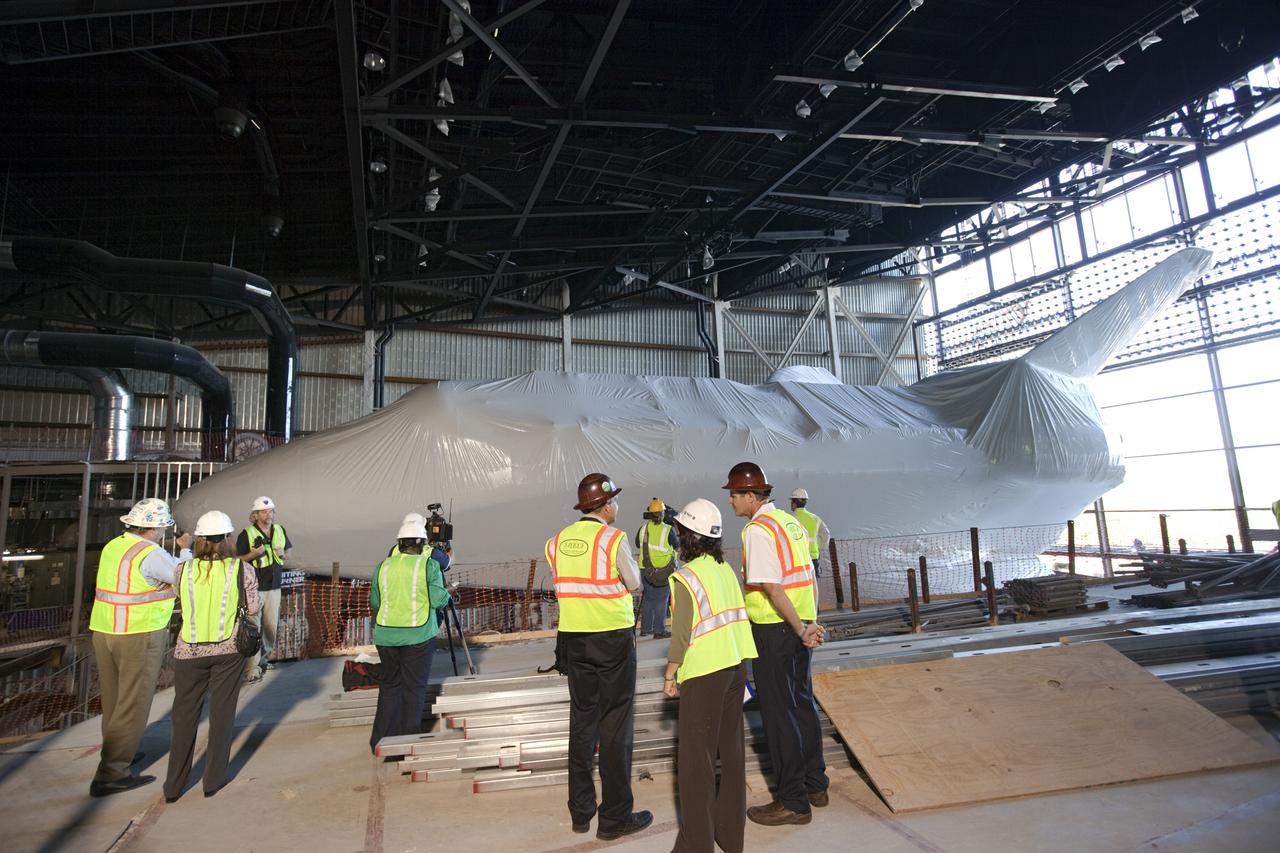 CAPE CANAVERAL, Fla. – Members of the media get an up close view of space shuttle Atlantis in her new home at the Kennedy Space Center Visitor Complex in Florida. The shuttle is wrapped in a protective plastic to protect it from dust and debris while being prepared for display. Atlantis was lifted 26 feet from the ground level and slowly tilted to exactly a 43.21 angle to its portside to allow optimum viewing of the vehicle with its payload bay doors open.    Atlantis is being prepared for display in the new 90,000-square-foot facility under construction at the visitor complex which is managed by Delaware North Companies Parks & Resorts. Photo credit: NASA/Dimitri Gerondidakis