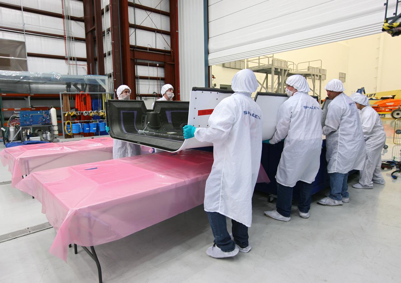 CAPE CANAVERAL, Fla. – Workers lift a solar array fairing at the processing hangar used by Space Exploration Technologies, or SpaceX, at Cape Canaveral Air Force Station, Fla. The fairings are to be installed on the Dragon spacecraft undergoing launch preparations inside the hangar. The spacecraft will launch on the upcoming SpaceX CRS-2 mission. The flight will be the second commercial resupply mission to the International Space Station by SpaceX. NASA has contracted for a total of 12 commercial resupply flights from SpaceX and eight from the Orbital Sciences Corp. Photo credit: NASA/Kim Shiflett