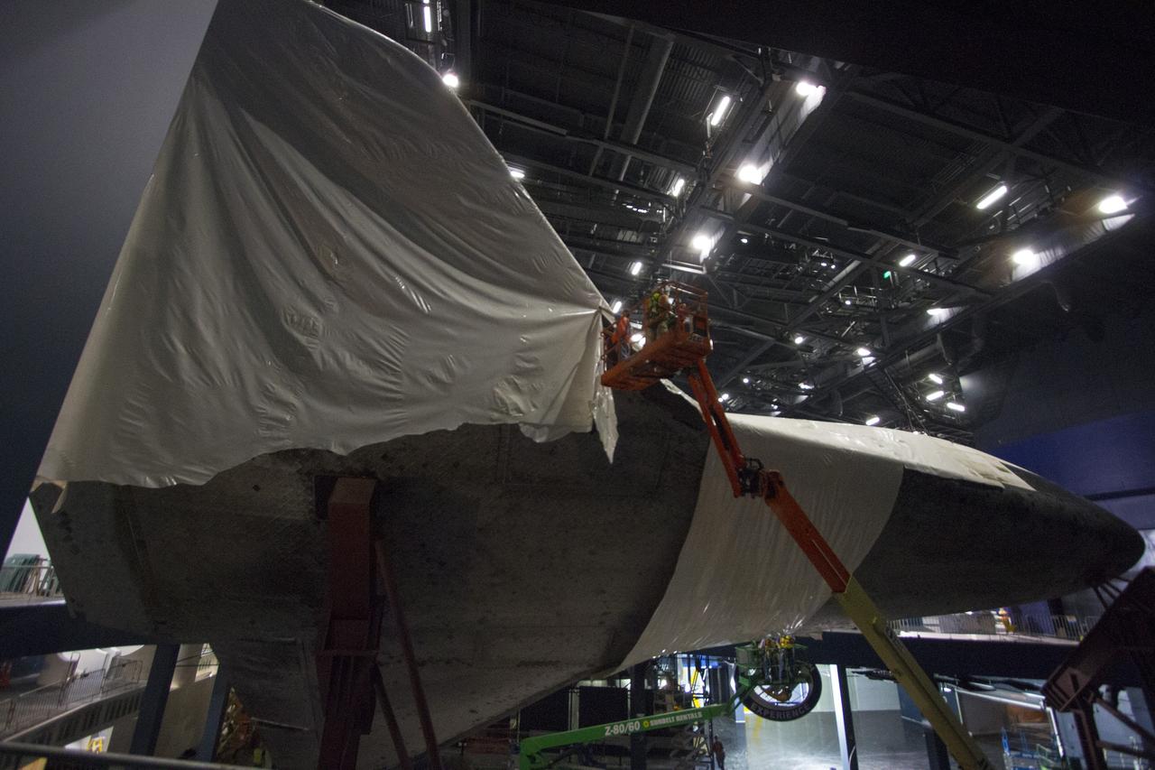 CAPE CANAVERAL, Fla. -- At the Kennedy Space Center Visitor Complex in Florida, construction crews remove 16,000 square feet of plastic shrink-wrap from the space shuttle Atlantis. The spacecraft was enclosed in the plastic shrink-wrap since November of last year to protect the artifact from dust and debris during construction of the 90,000-square-foot facility. Last November, the space shuttle Atlantis made its historic final journey to its new home, traveling 10 miles from the Kennedy Space Center's Vehicle Assembly Building to the spaceport's visitor complex. The new $100 million "Space Shuttle Atlantis" facility will include interactive exhibits that tell the story of the 30-year Space Shuttle Program and highlights the future of space exploration. The "Space Shuttle Atlantis" exhibit scheduled to open June 29, 2013.Photo credit: NASA/Cory Huston